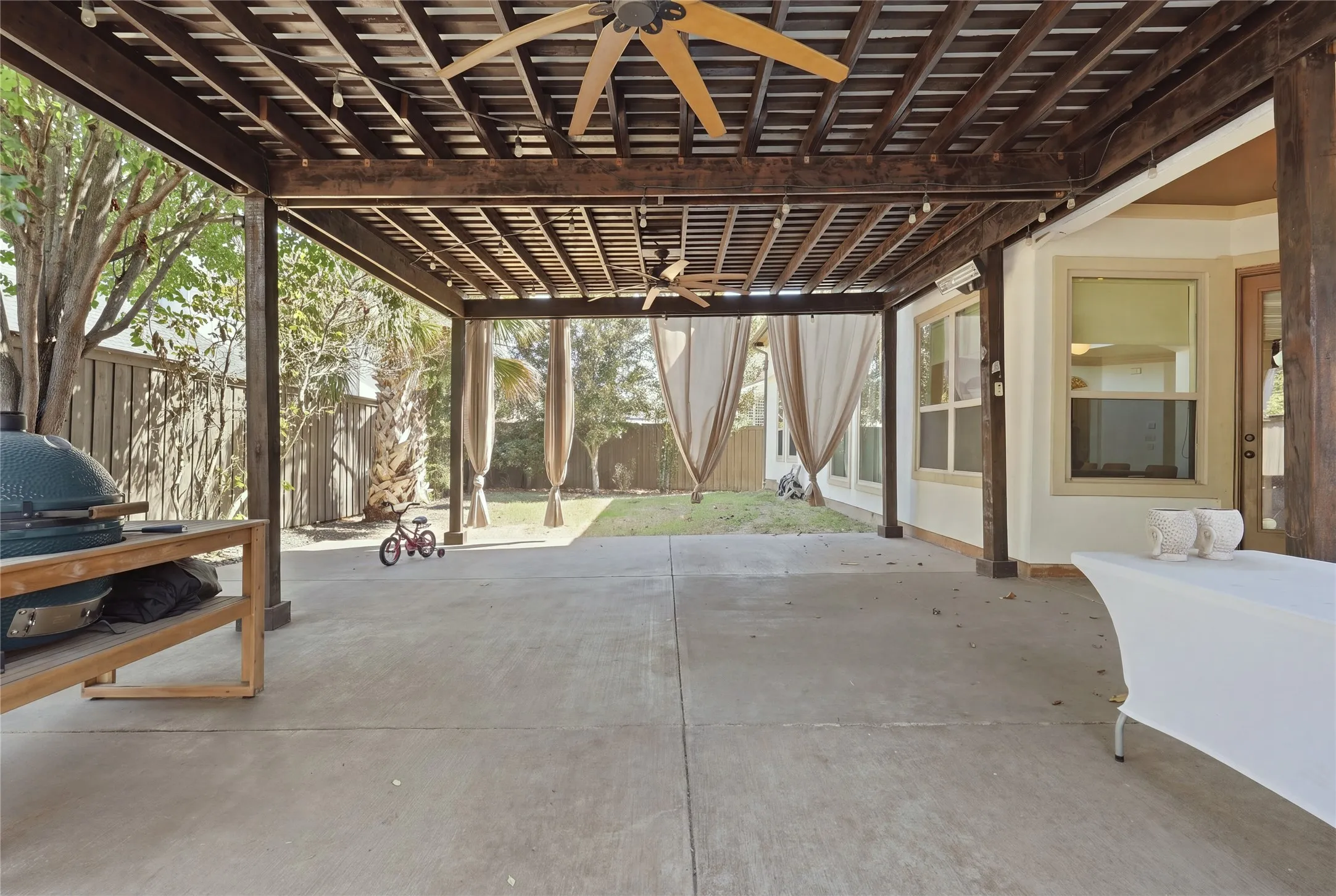 Expansive concrete patio featuring a wood pergola and ceiling fans