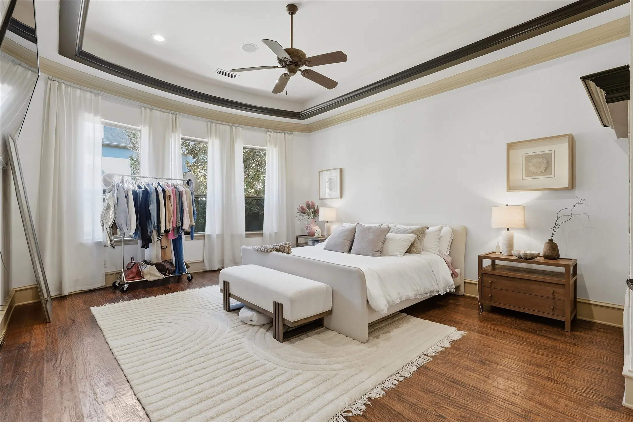 Tray ceiling with crown molding, ceiling fan, wood-finish flooring, and multiple windows with drapery