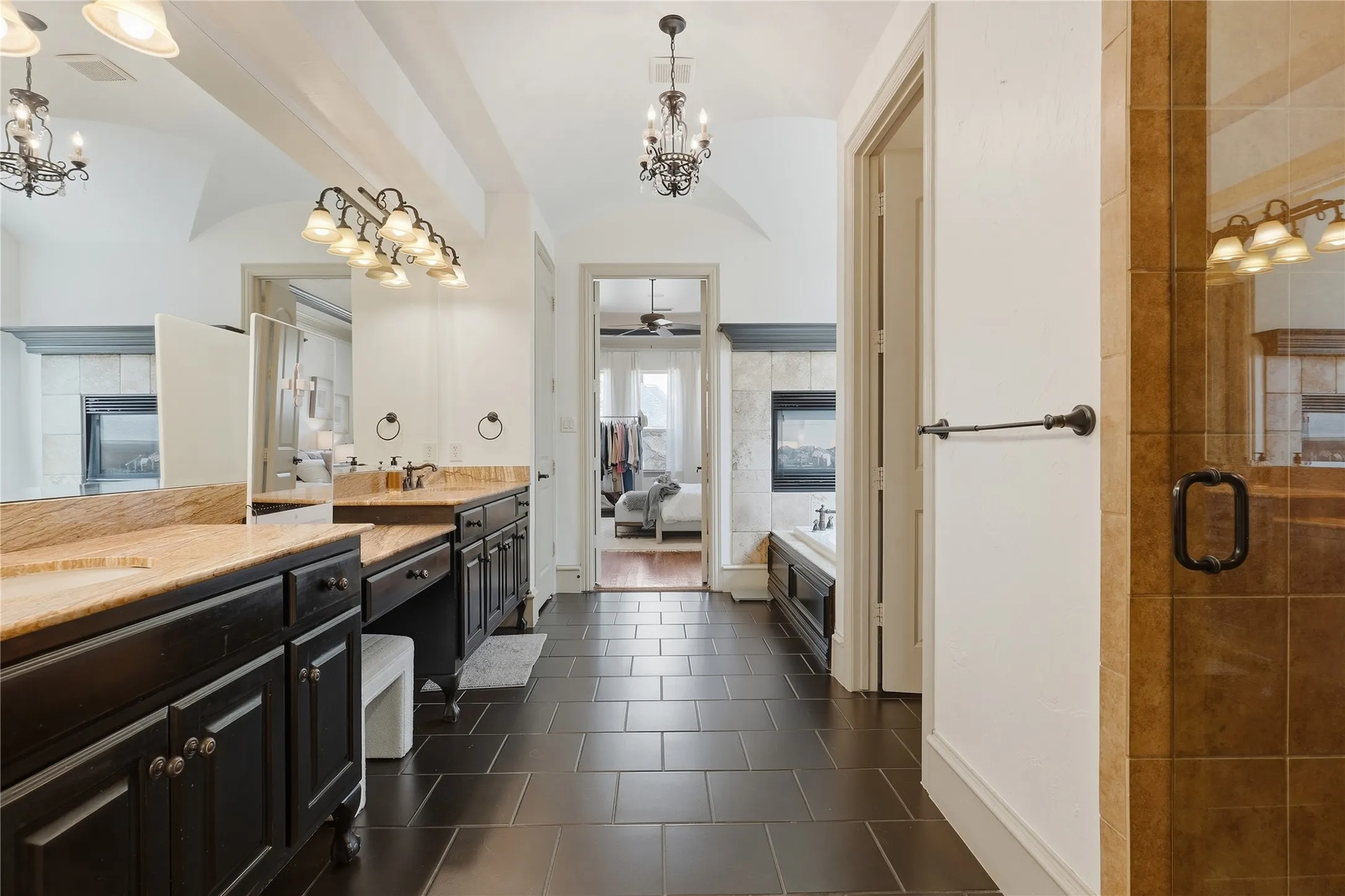 Dual vanities with stone countertops, dark wood cabinetry, tile flooring, an attached shower enclosure with tile surround, and a built-in fireplace feature