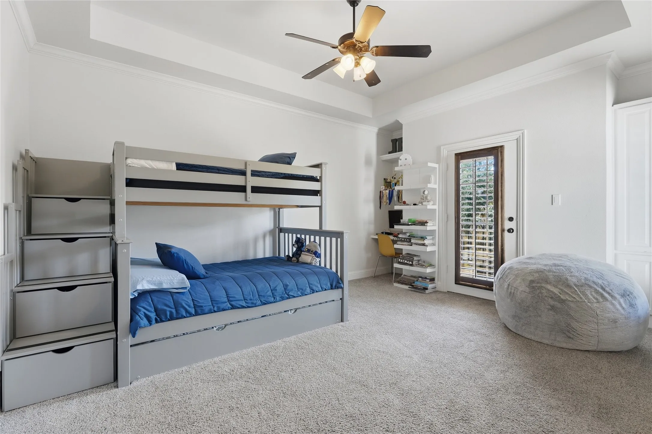 Tray ceiling, ceiling fan, white built-in cabinetry, recessed shelving, and a door with louvered glass