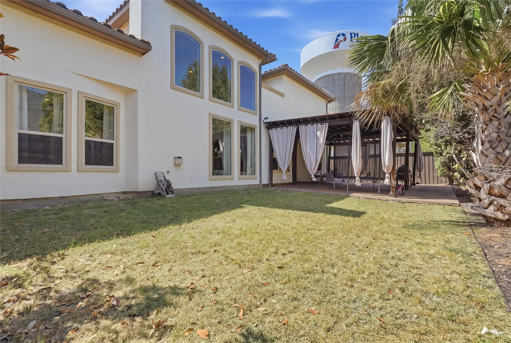 Rear exterior featuring arched windows, multiple windowpanes, a covered patio with a dark wood pergola, and a privacy fence