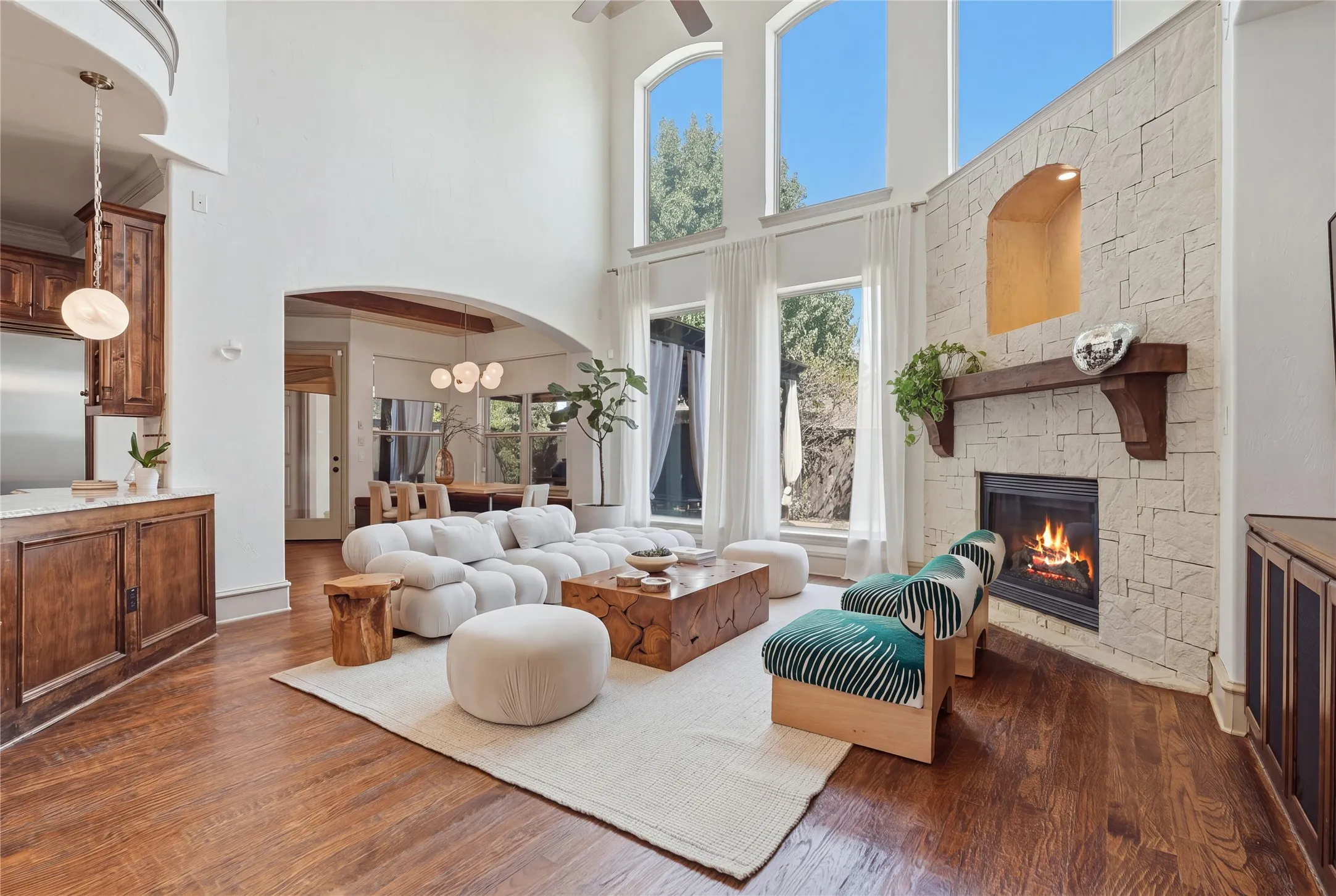 Two-story living area with wood-finish flooring, a stone-clad fireplace, and multiple arched windows