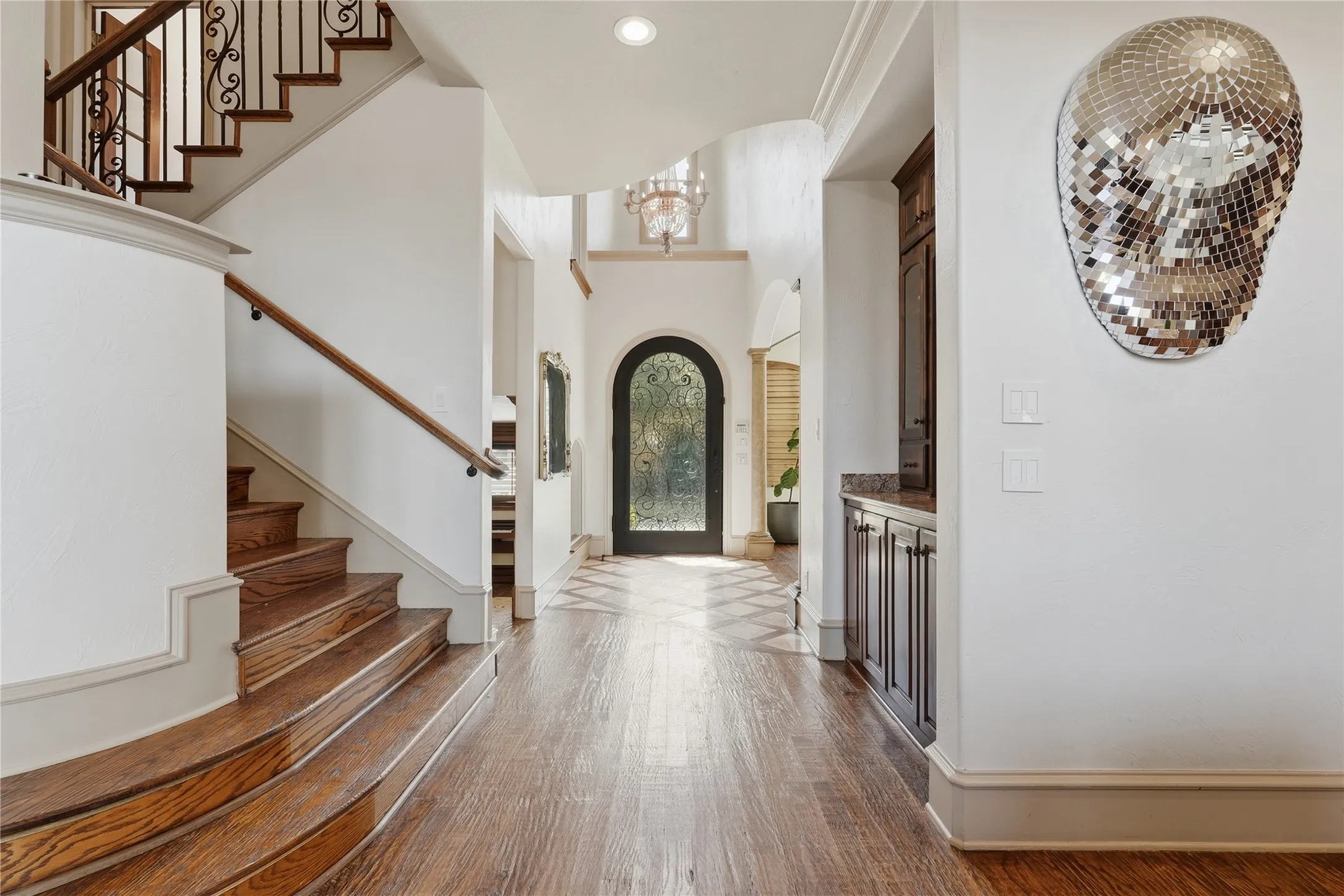 Hardwood flooring, arched doorway, grand staircase with wrought iron railing, recessed lighting, built-in cabinetry with stone countertop