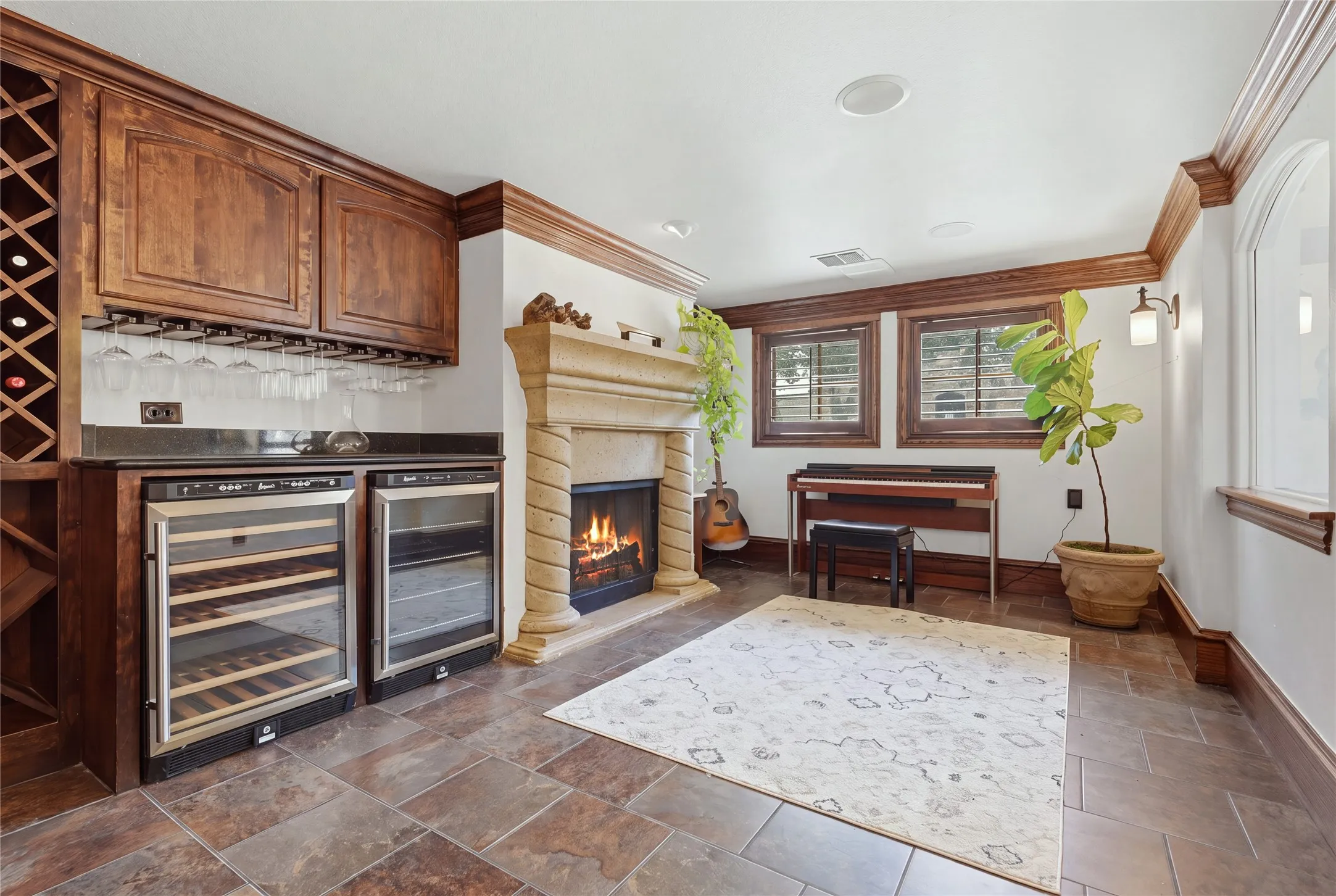 Built-in wet bar with wine storage and two beverage refrigerators, stone fireplace, and tile flooring