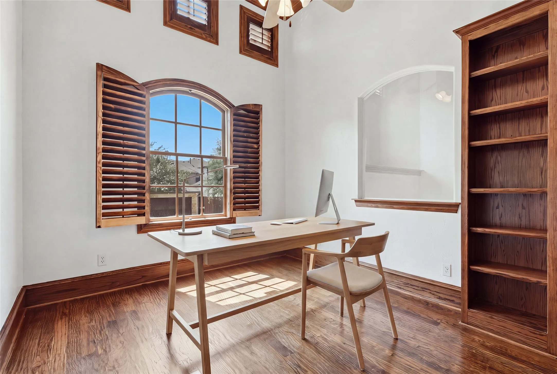 Wood-finish flooring with coordinating wood trim, an arched window with wood shutters, and built-in wood shelving