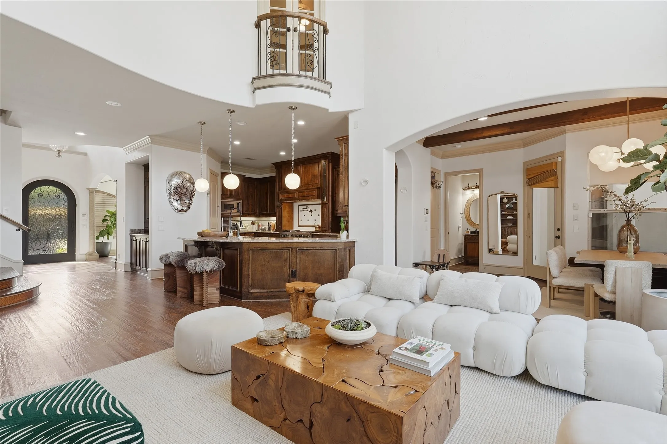 Expansive open-concept living area featuring high ceilings, wood-finish flooring, a kitchen island with pendant lighting, and an arched entry to a dining space with exposed ceiling beams