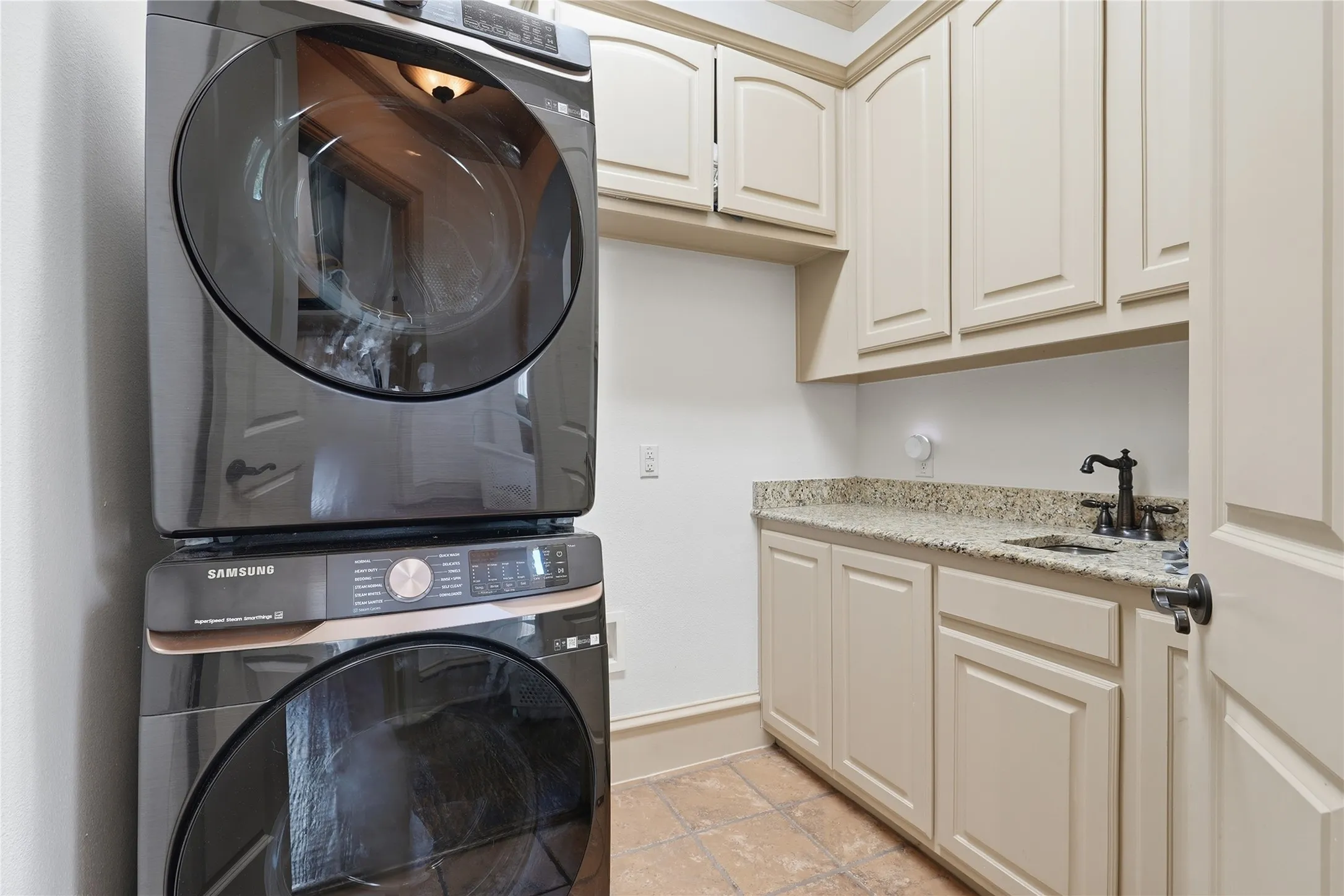 Integrated laundry area featuring neutral cabinetry, granite-finish countertop, and a built-in sink with a dark bronze-finish faucet