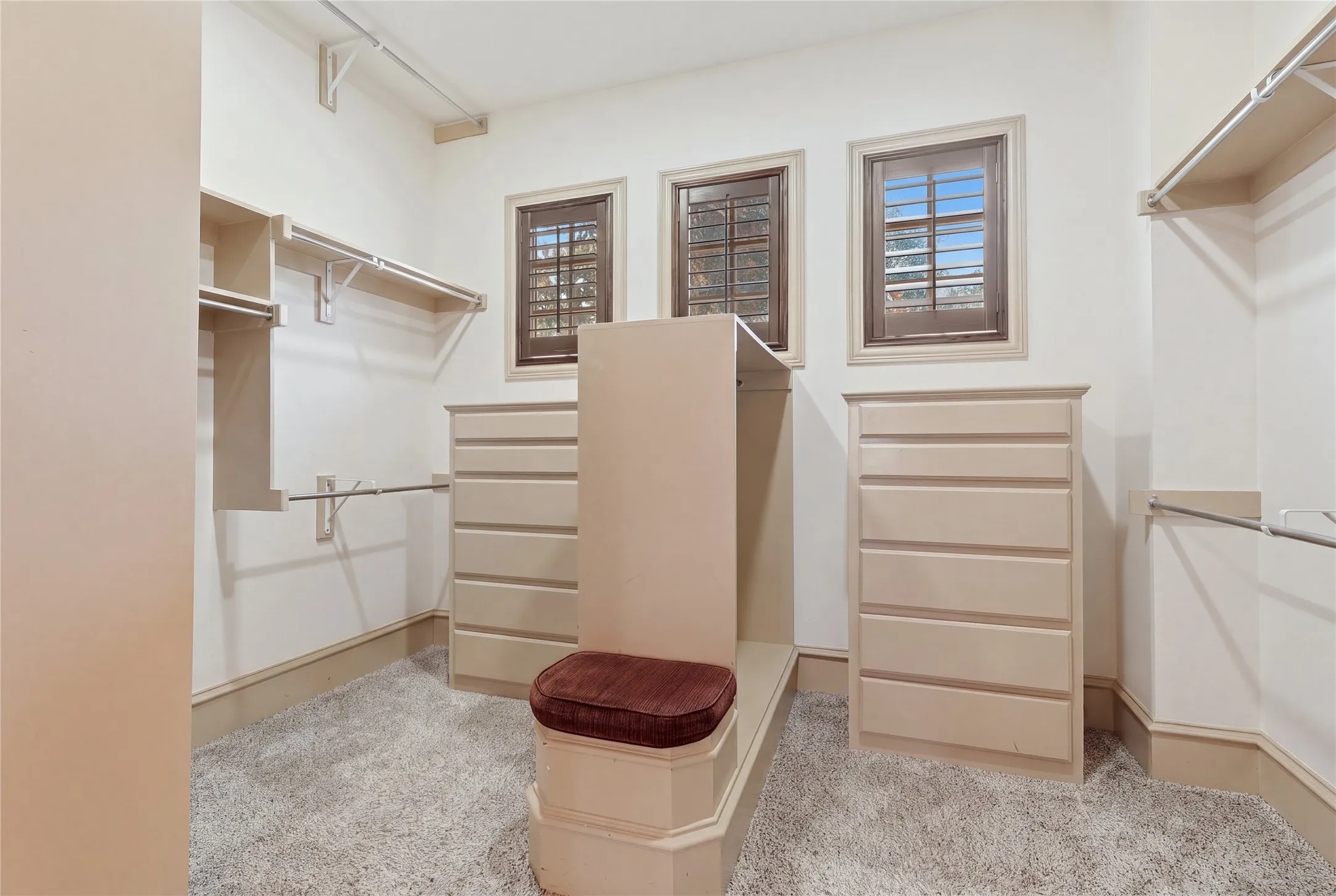 Light-toned wall paint, built-in shelving, multiple storage rods, built-in dresser units, and three windows with shutters