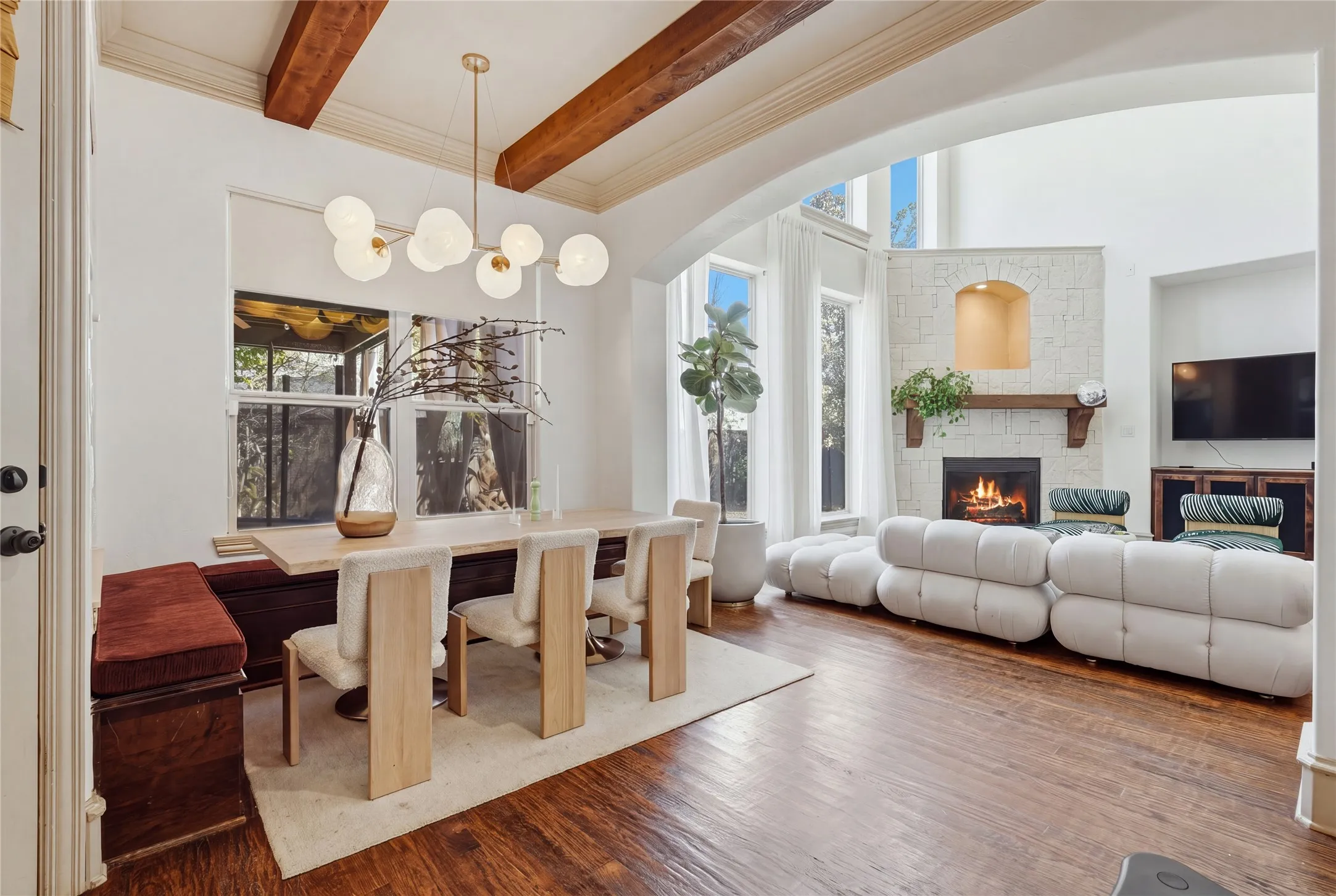 Vaulted ceiling with exposed wood beams, hardwood flooring, fireplace with stone surround, and an arched entryway