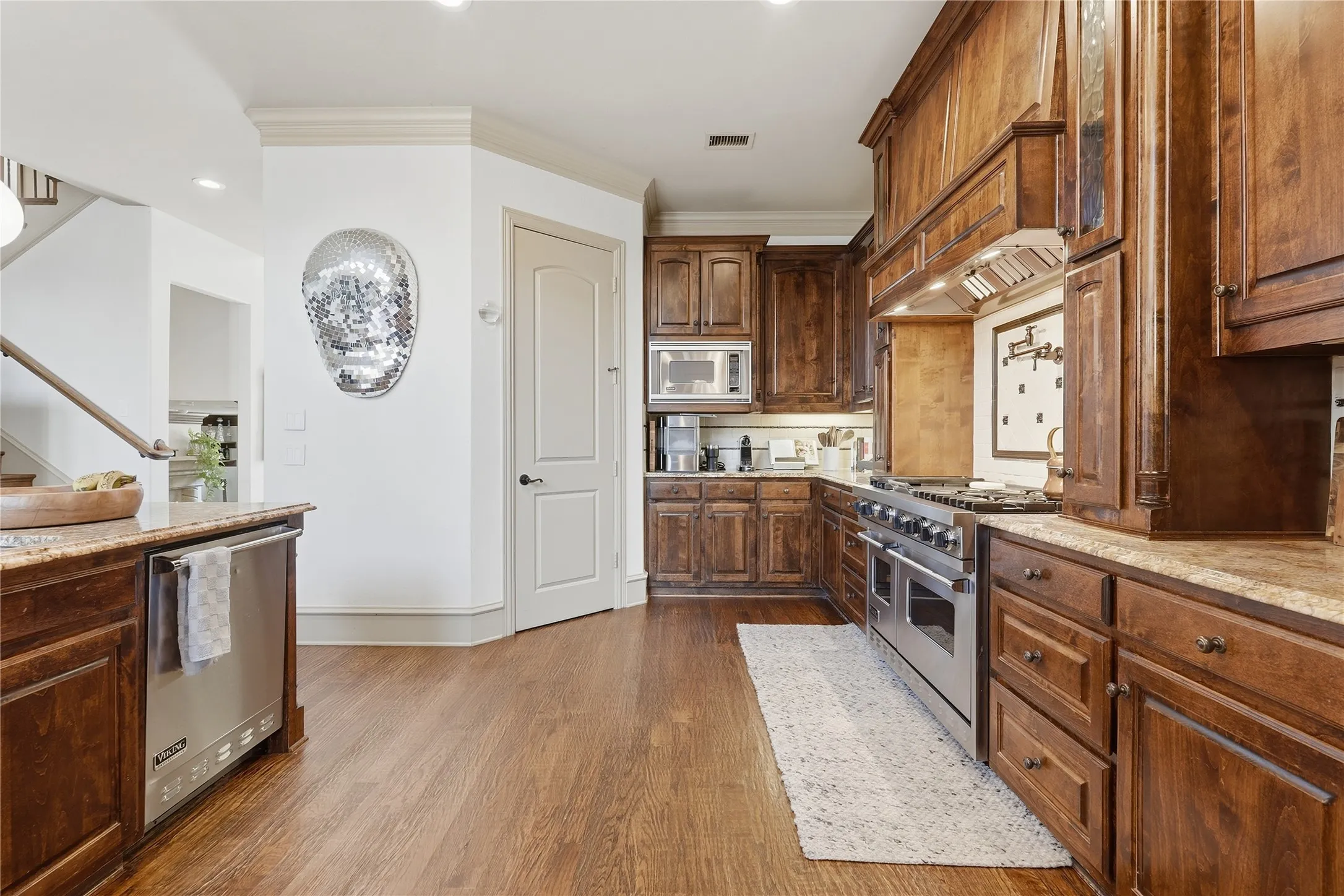 Gourmet kitchen featuring wood-finish cabinetry, stainless steel appliances, stone countertops, and wood-finish flooring