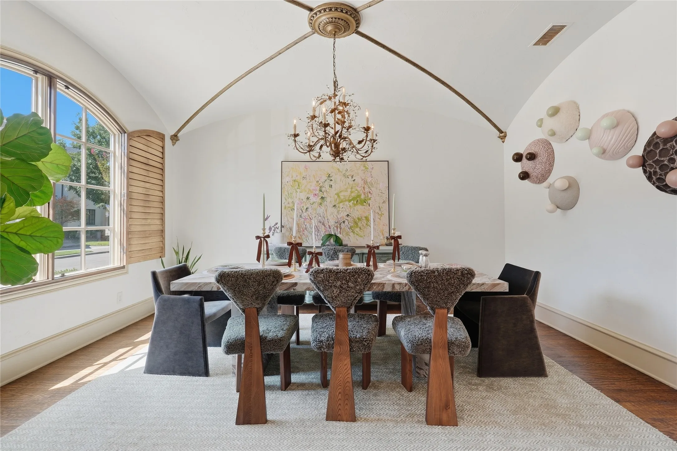Vaulted ceiling with decorative arch details, arched window with wood shutters, and wood-finish flooring