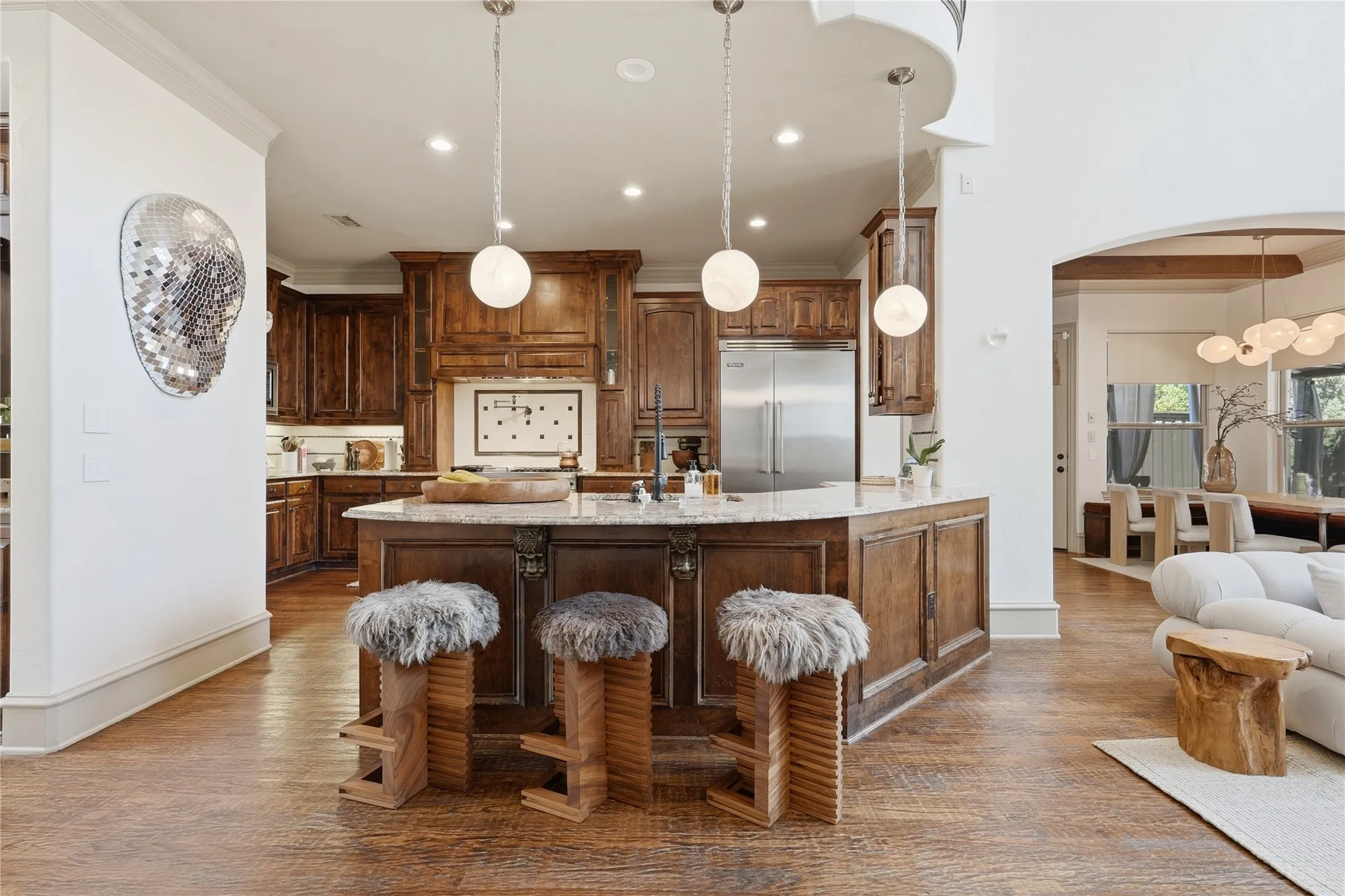 Wood-finish flooring throughout, kitchen island with built-in storage, stainless steel refrigerator, recessed lighting, and an arched doorway