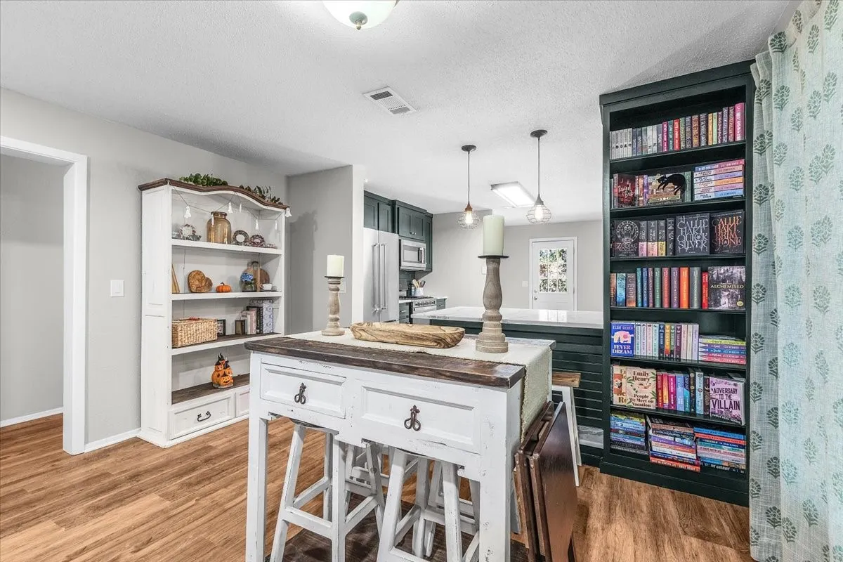 Wood-finish flooring throughout, custom built-in shelving, white painted cabinetry with wood-finish countertop, dark-painted built-in bookcase, and recessed lighting