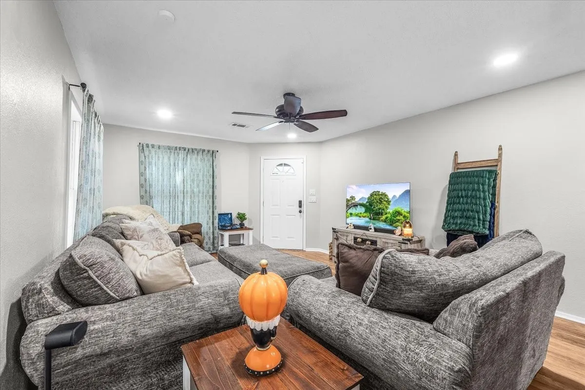 Recessed lighting illuminates the living space featuring wood-finish flooring and a white entry door with an arched window