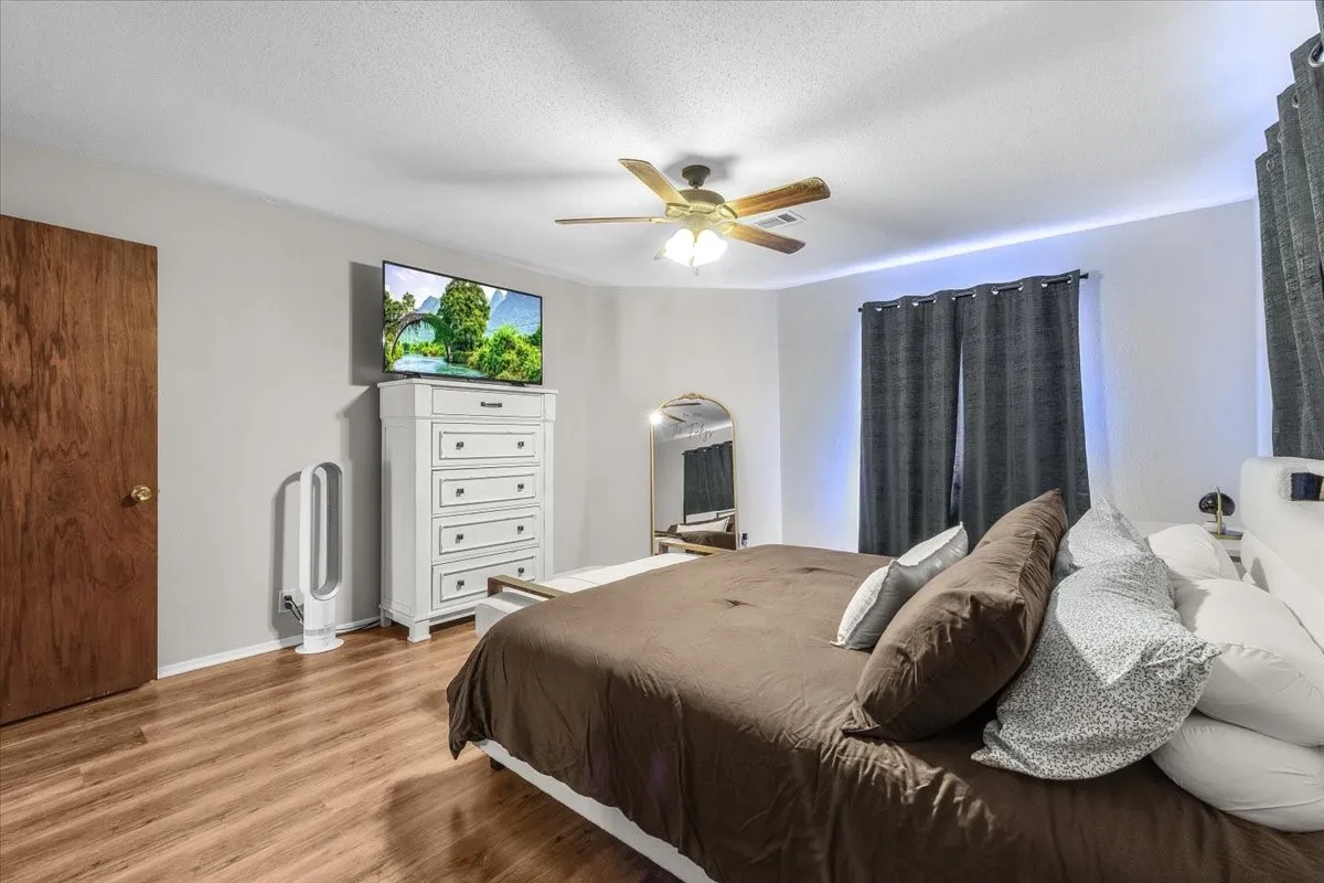 Wood-finish flooring, ceiling fan with integrated lighting, window with dark drapes, and a wood-panel door