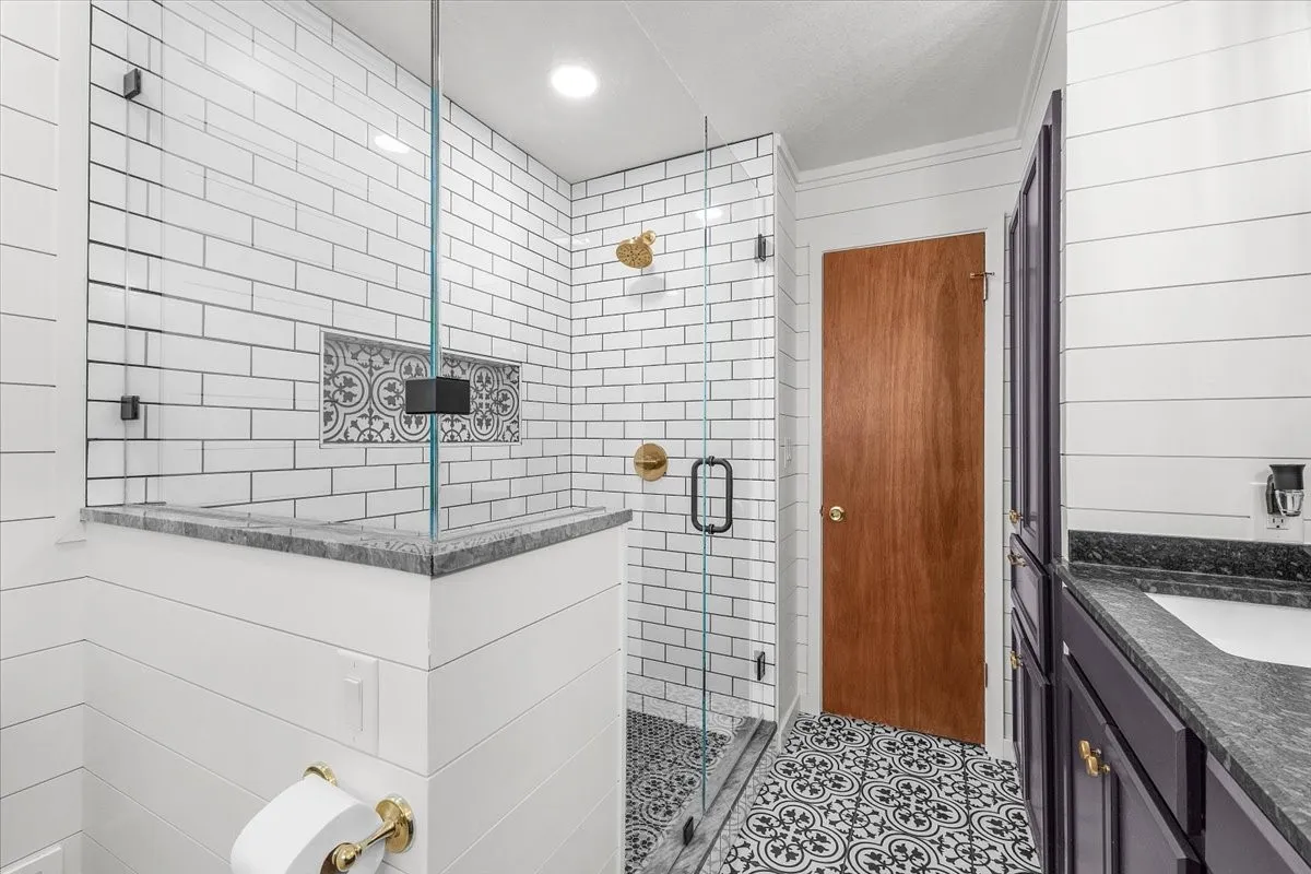 Glass-enclosed shower with subway tile surround, decorative tile shower niche, and patterned floor tile