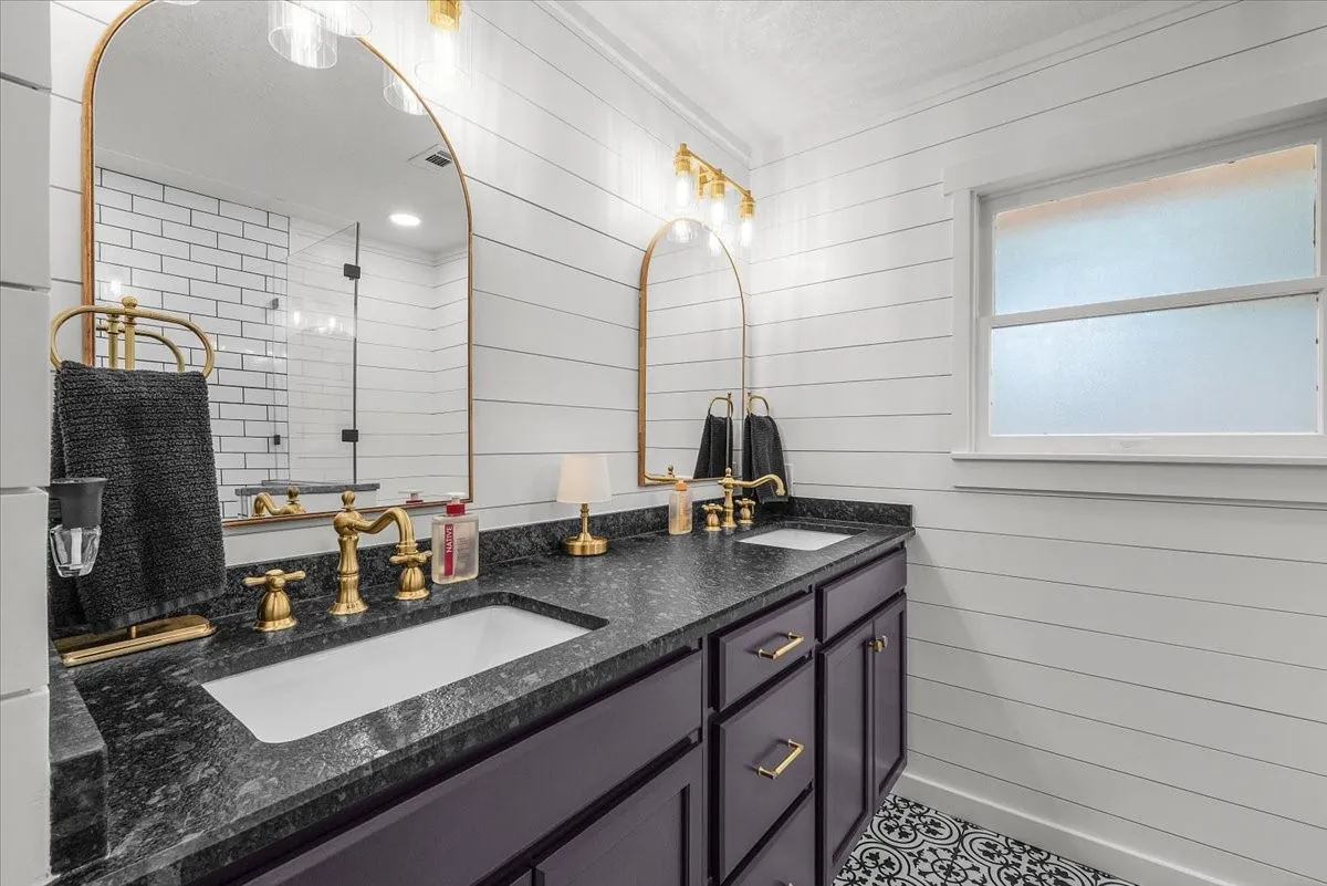 Full bath dual vanity with dark stone granite countertop, undermount sinks, and brass-finish fixtures