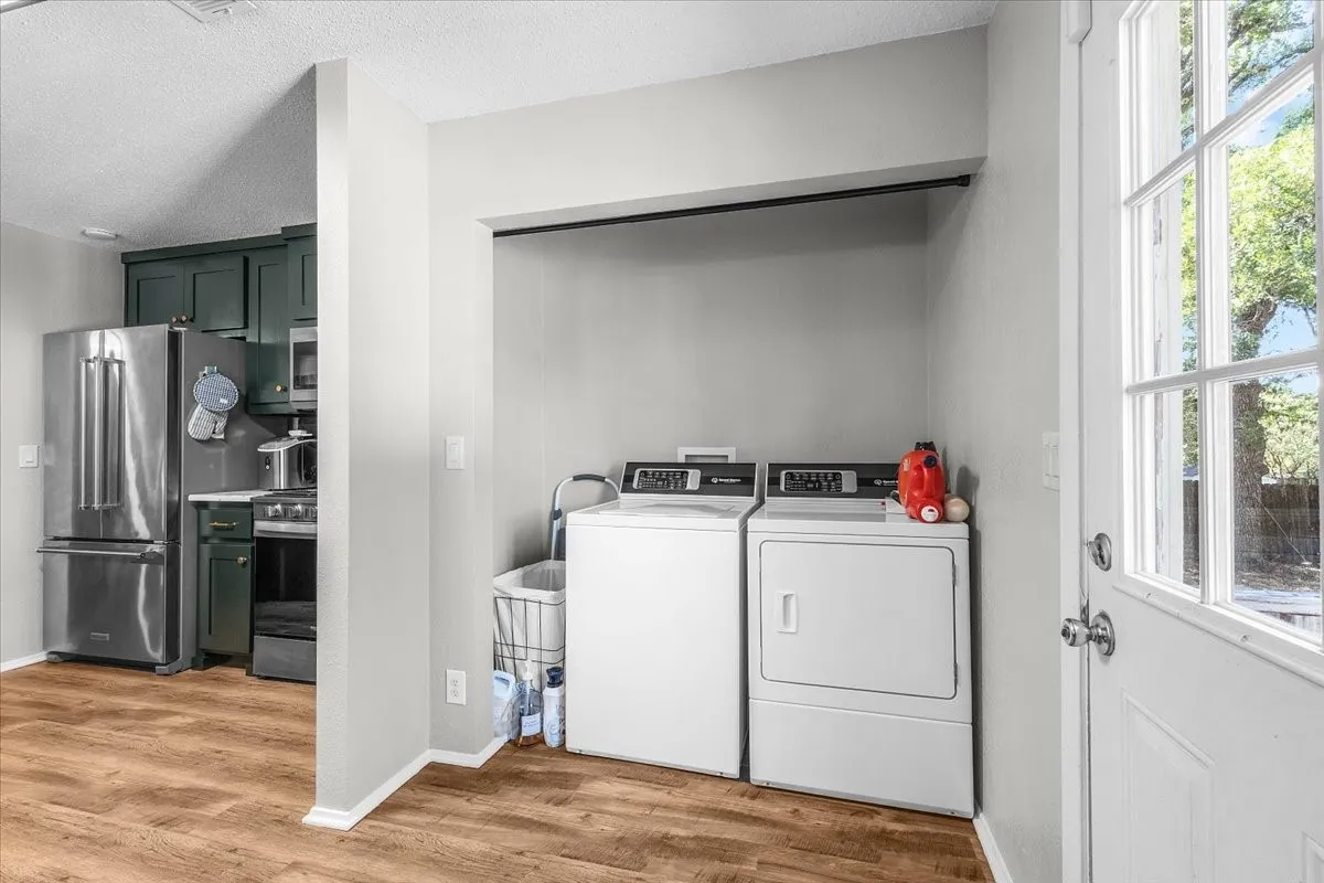Full size laundry area with built-in hanging rod, wood-finish flooring, and an adjacent kitchen