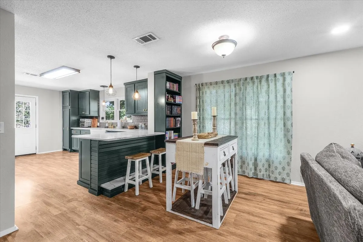 Wood-finish flooring, dark-toned cabinetry, built-in shelving, white countertop, and pendant lighting