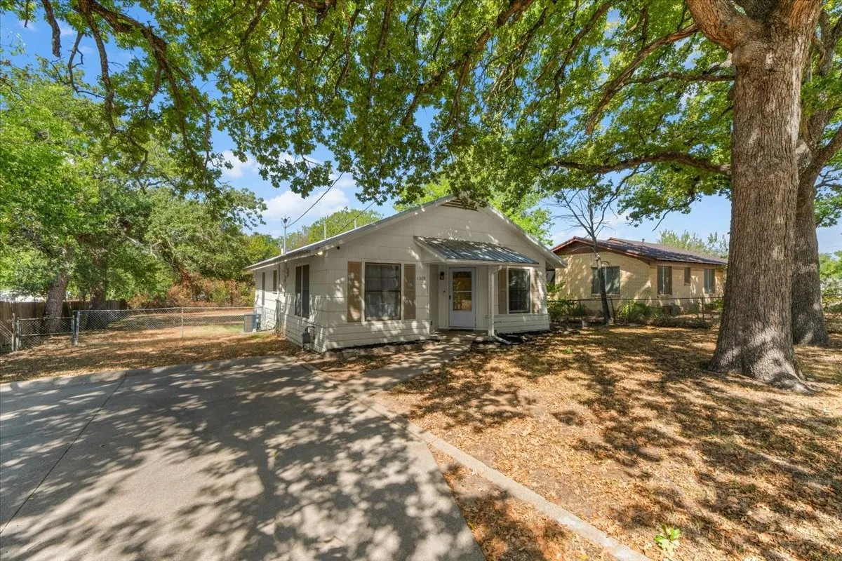 White exterior siding, a covered front porch, and mature trees providing natural shade