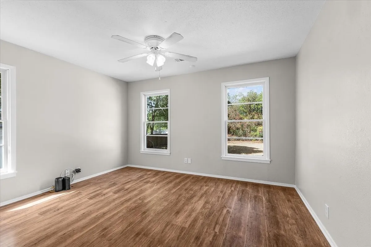 Wood-finish flooring, multiple windows, ceiling fan with integrated lighting, and neutral wall tones