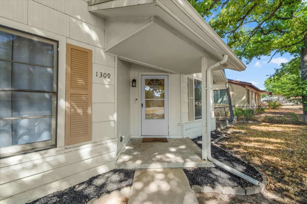 White siding exterior with a covered entry, decorative shutters, and a front entry door with an arched window insert