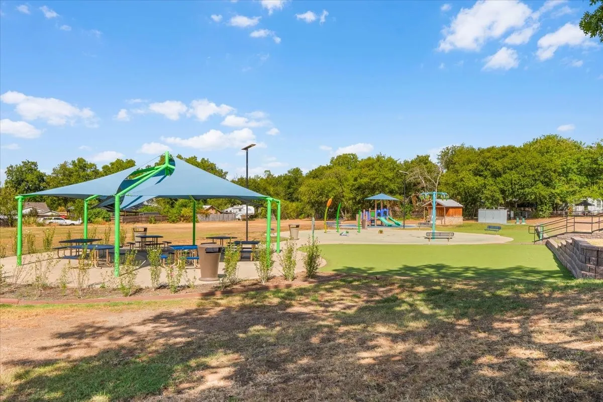Community park with a shade structure, multiple picnic tables, a playground, and artificial turf surfacing only 1 block away