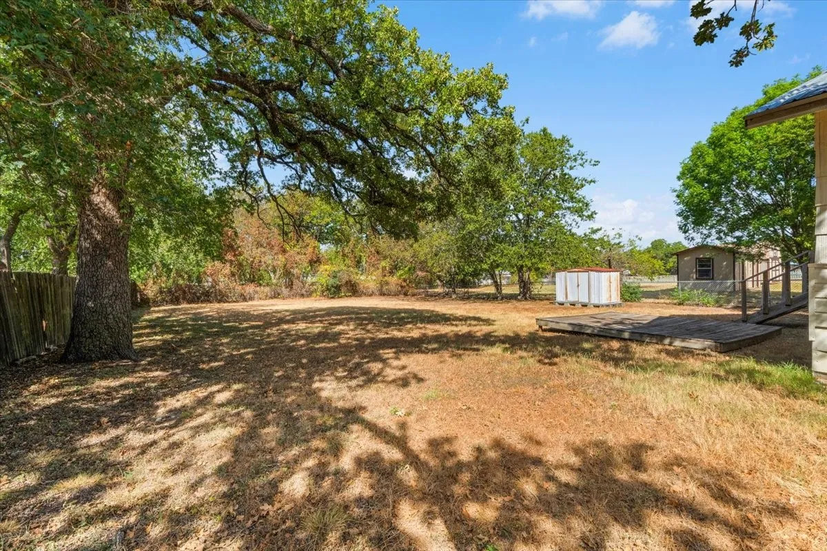 Expansive backyard with mature trees, a wooden deck, and a detached storage shed