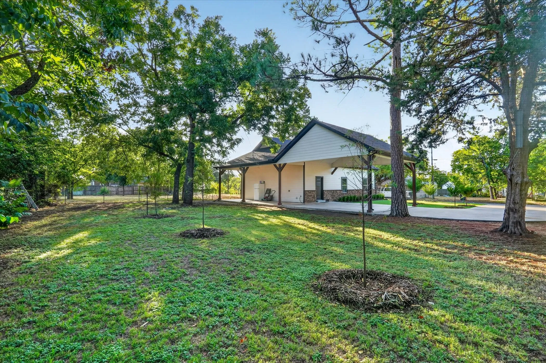 Expansive grassy yard with mature trees, a paved driveway, and a detached structure featuring stone veneer accents and a covered porch