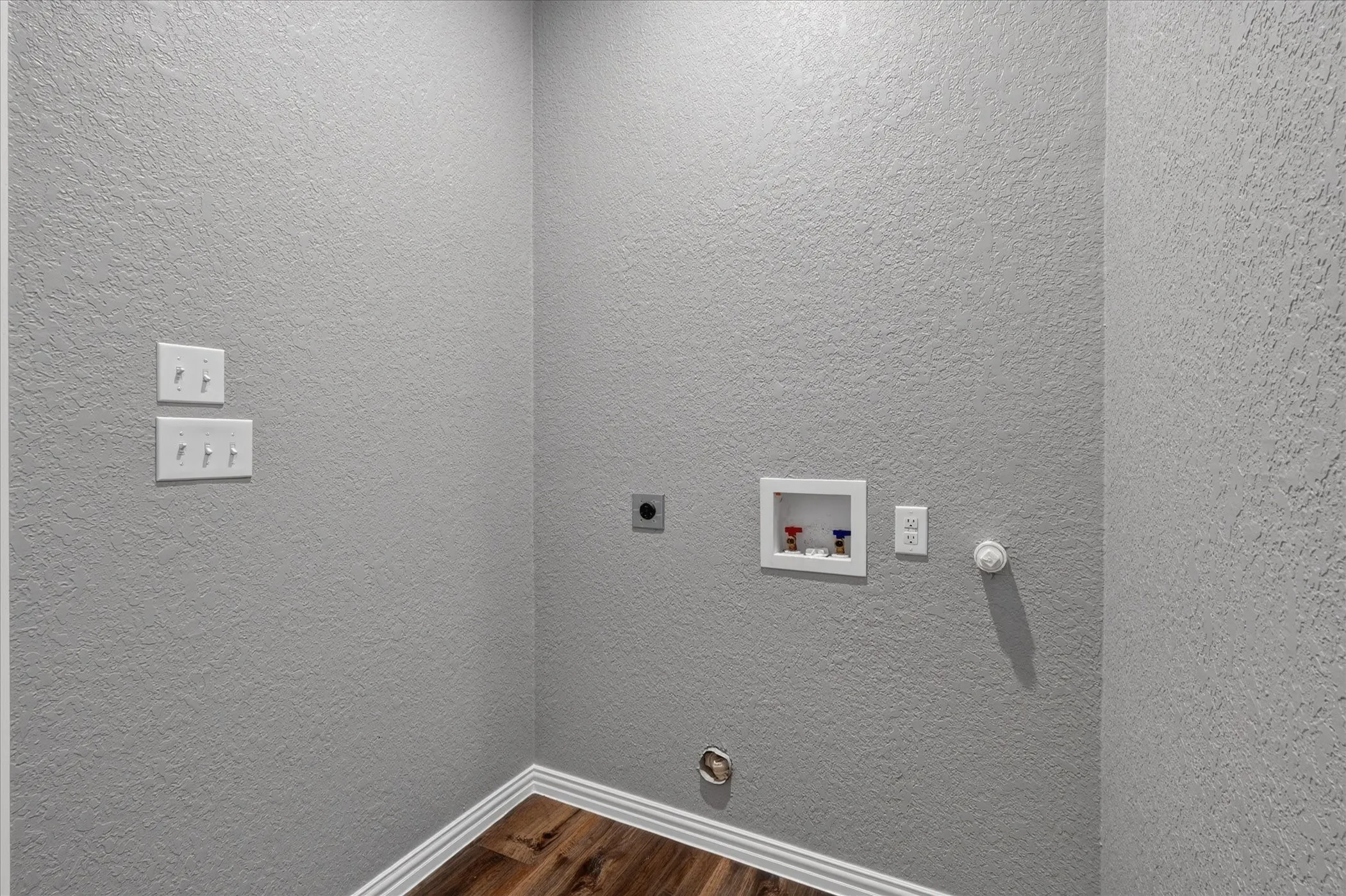 Wood-finish flooring with white trim, gray textured walls, and laundry hookups