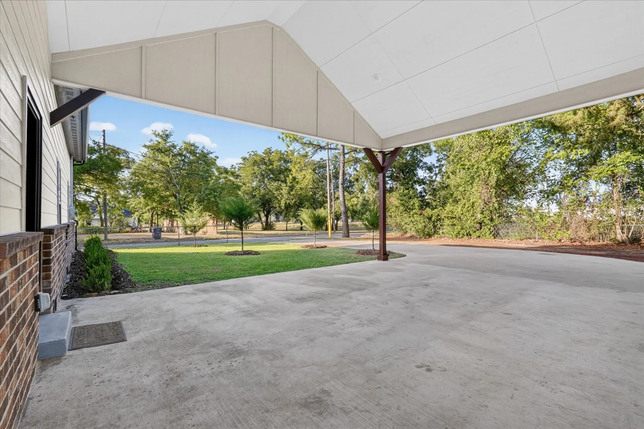 Paved carport with a pitched white ceiling, supported by a stained wood post, featuring a brick and siding exterior and a manicured lawn