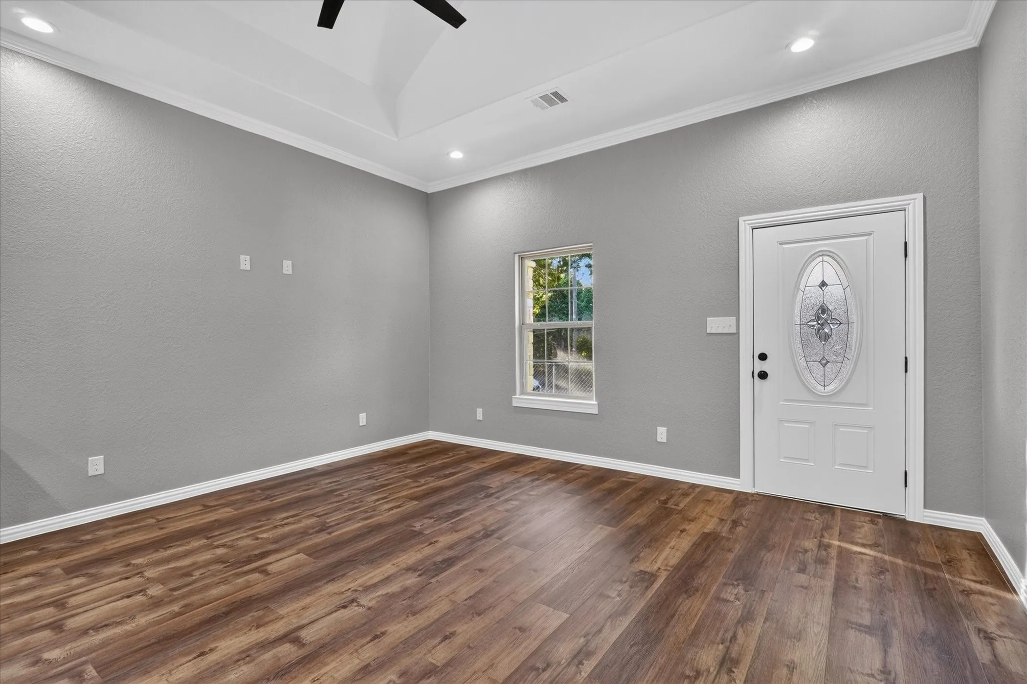 Wood-finish flooring, tray ceiling, recessed lighting, white trim, and a decorative glass-insert door