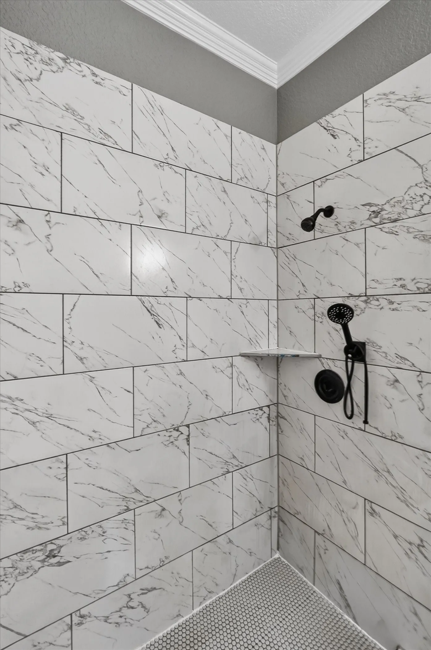 Shower with large format subway tile walls, corner shelf, handheld shower fixture, and penny tile flooring