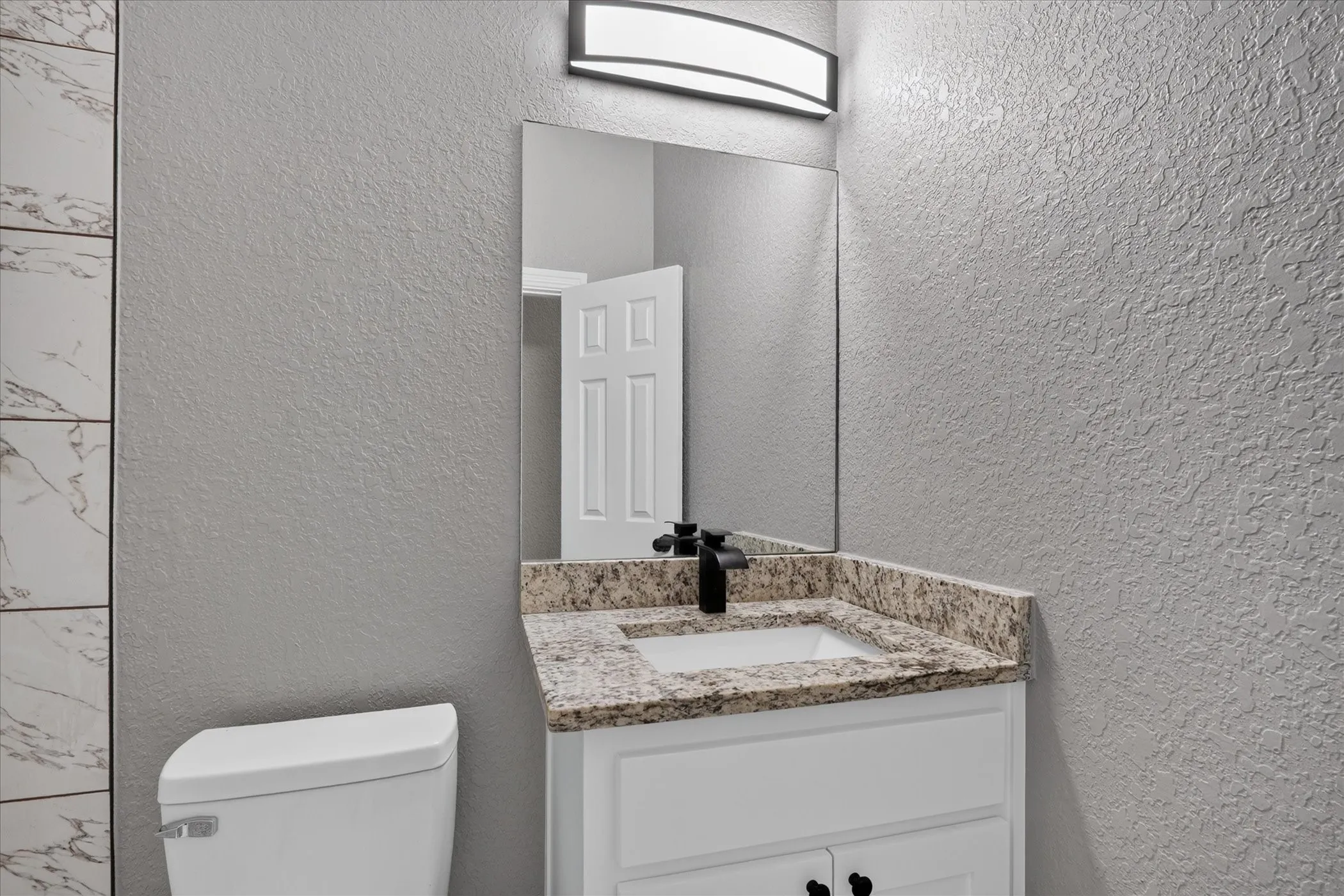 Vanity with a granite-style countertop, white cabinetry, and matte black faucet