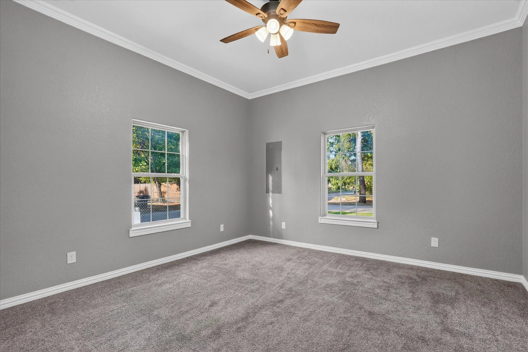 Carpeted room featuring dual windows, a ceiling fan with light kit, and crown molding