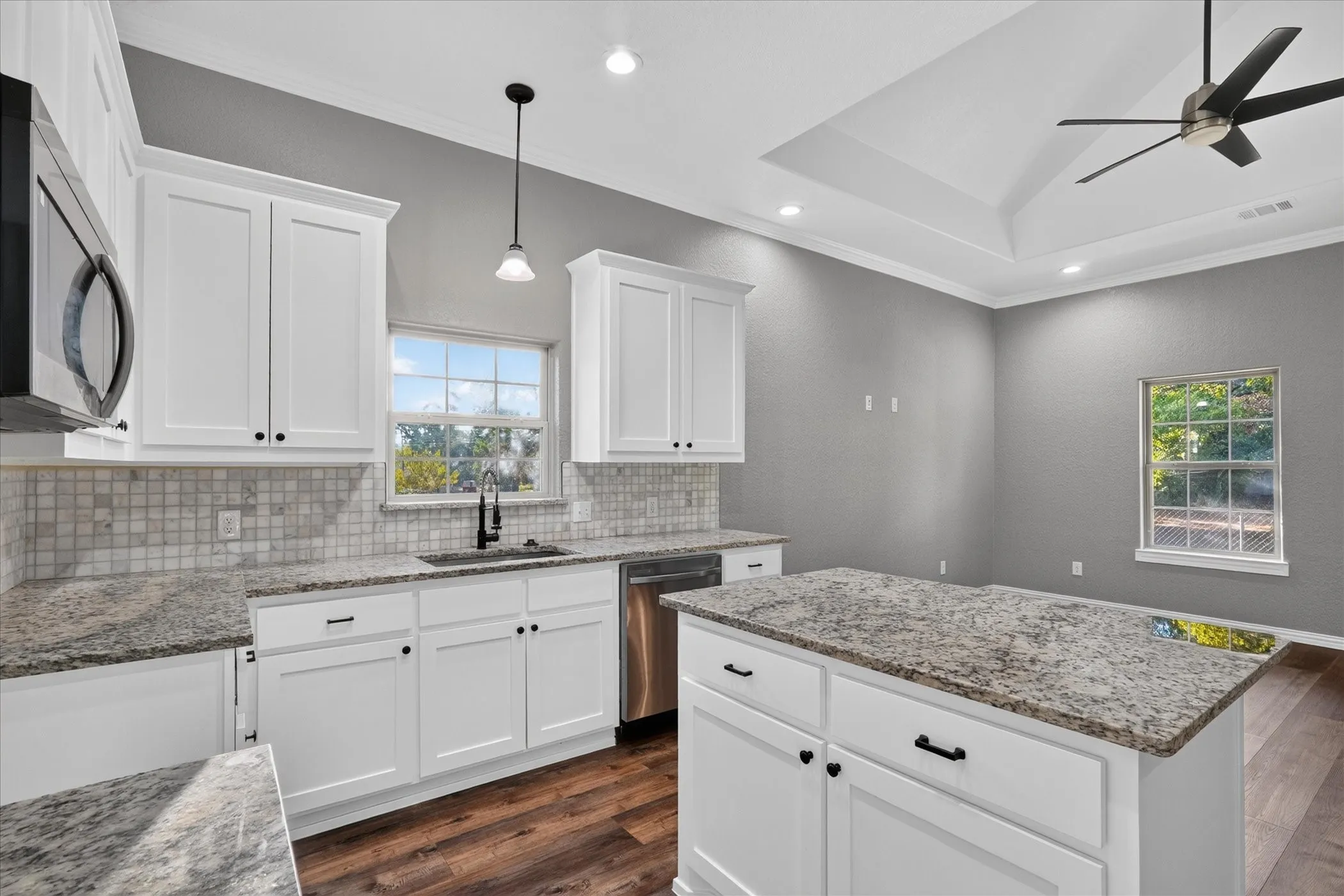 White shaker cabinetry, stone countertops, stainless steel appliances, wood-finish flooring, and a tray ceiling