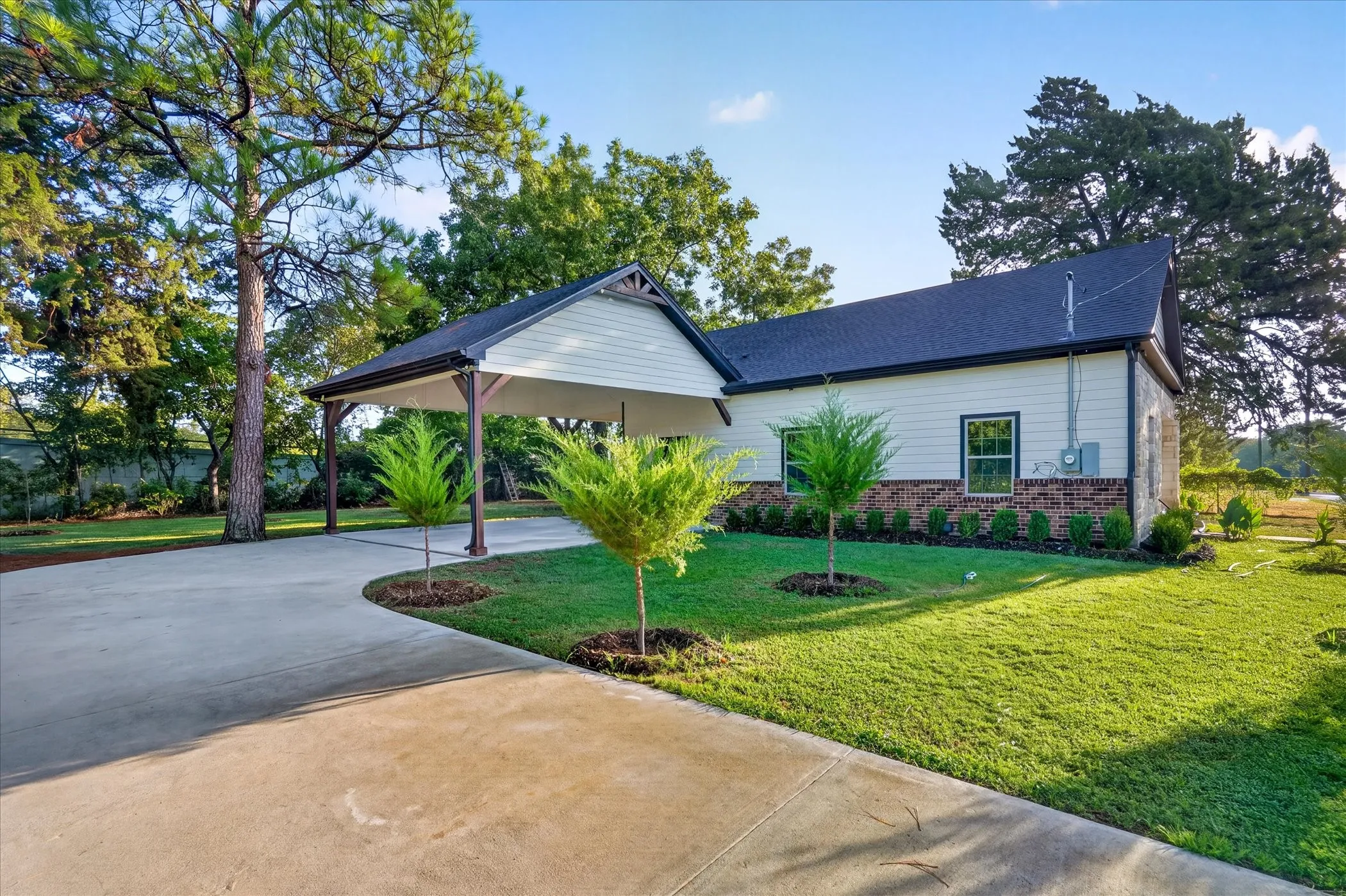 Exterior featuring a covered carport, concrete driveway, white siding, and a partial brick facade