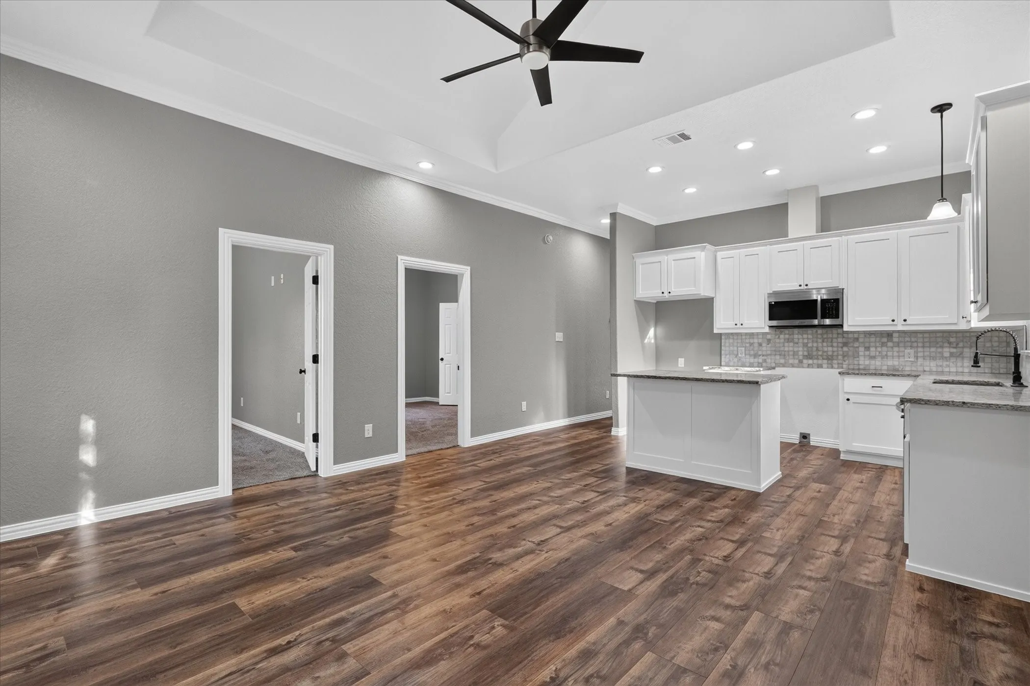 Vaulted ceiling with a ceiling fan, recessed lighting, wood-finish flooring, white cabinetry, and granite countertops