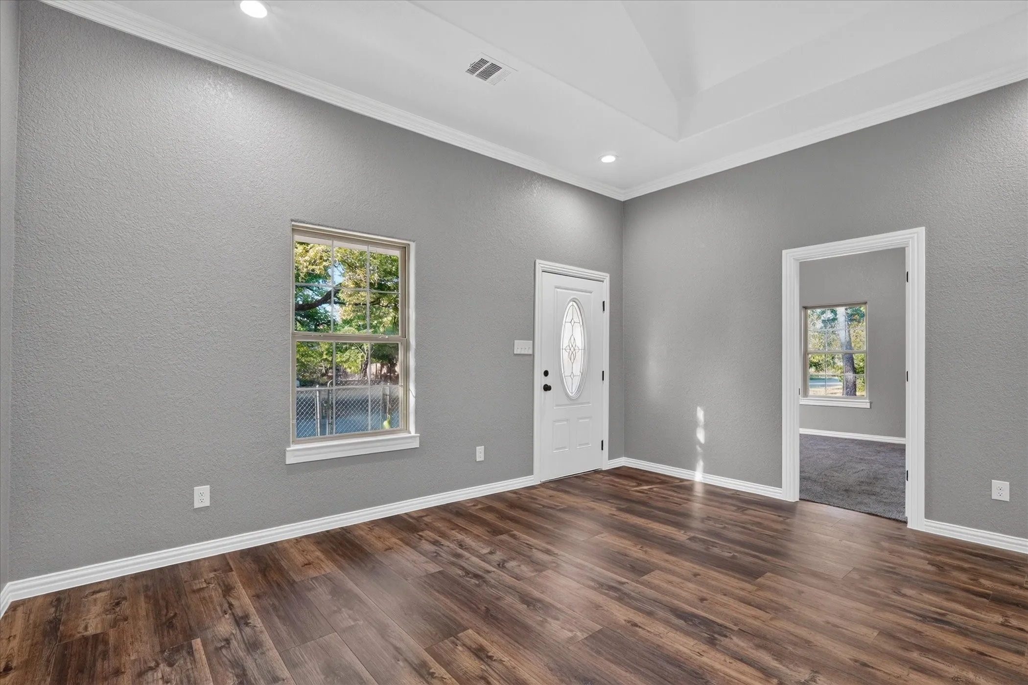 Wood-finish flooring, recessed lighting, tray ceiling, white trim, and a white front entry door with decorative glass insert