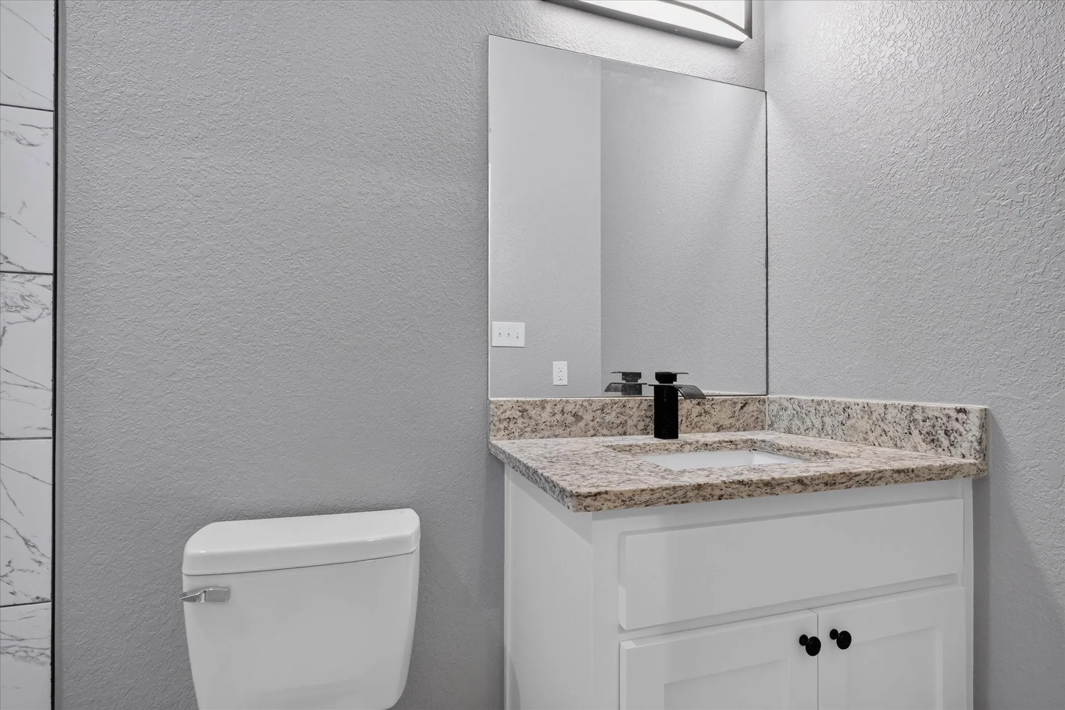 White vanity with granite countertop, integrated sink, and matte black faucet