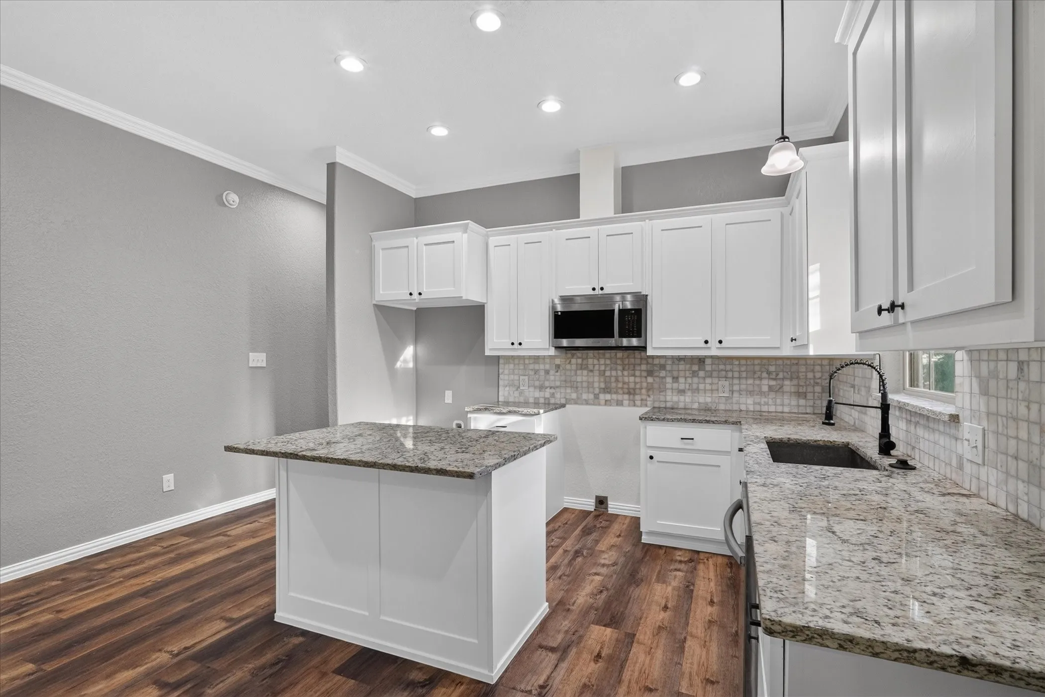 White cabinetry with dark hardware, stone countertops, stainless steel microwave, tile backsplash, and wood-finish flooring