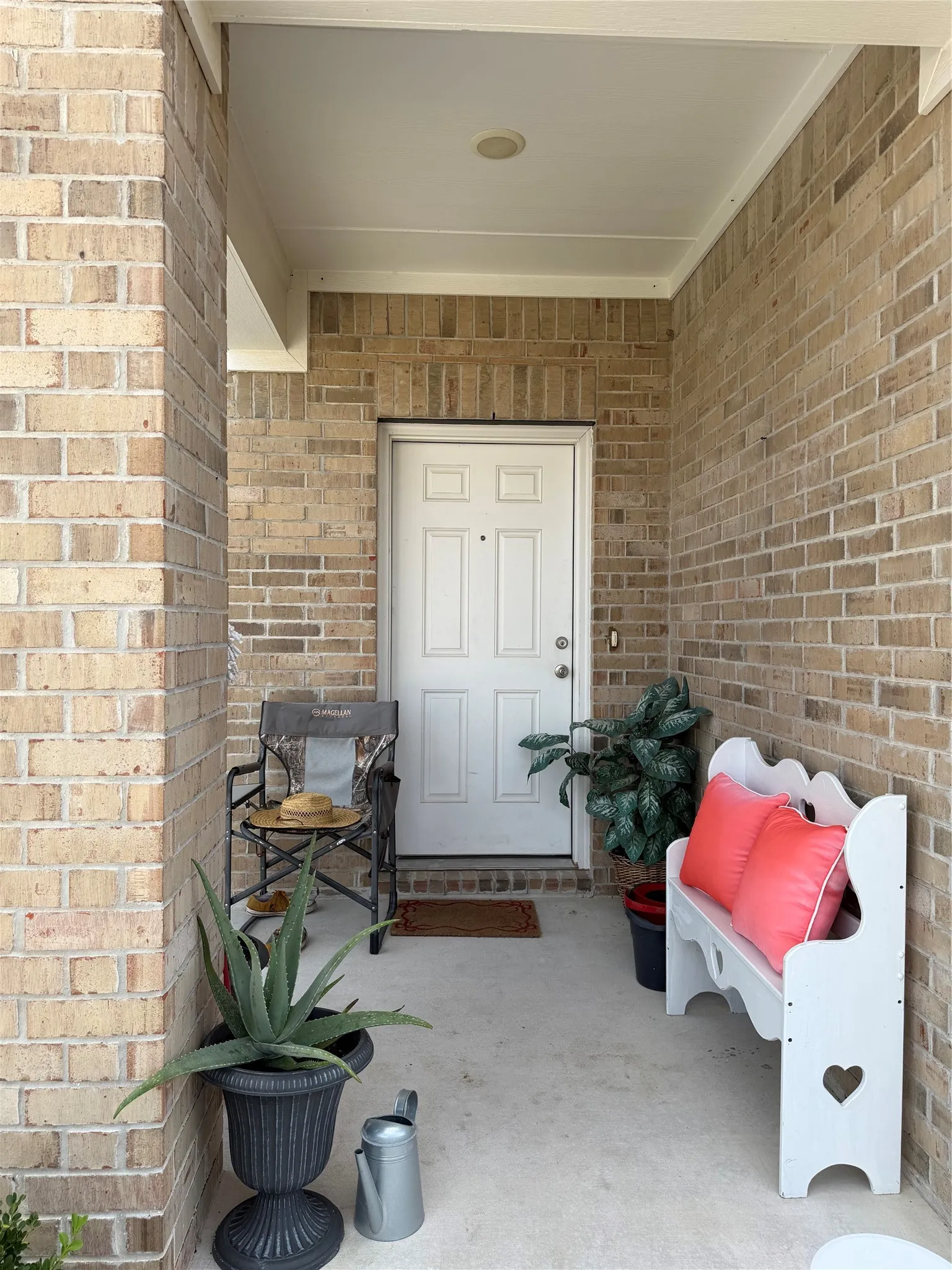 Covered concrete porch with brick exterior, white paneled entry door, and recessed lighting