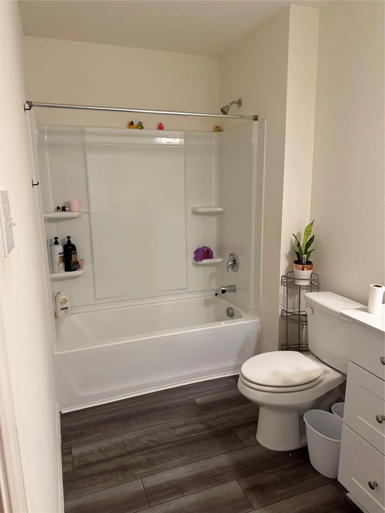 Bathroom featuring a combination tub/shower unit with a showerhead, wood-finish flooring, and a vanity cabinet with white drawers