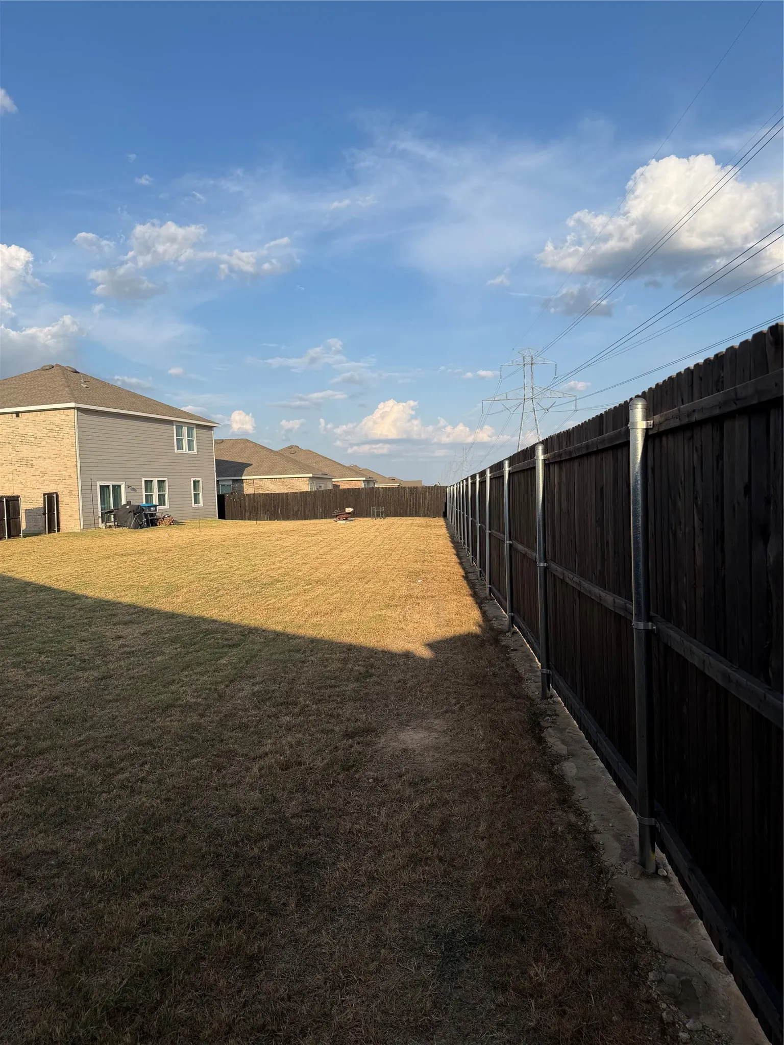 Expansive outdoor area featuring a wooden privacy fence, a concrete perimeter, and a grass lawn