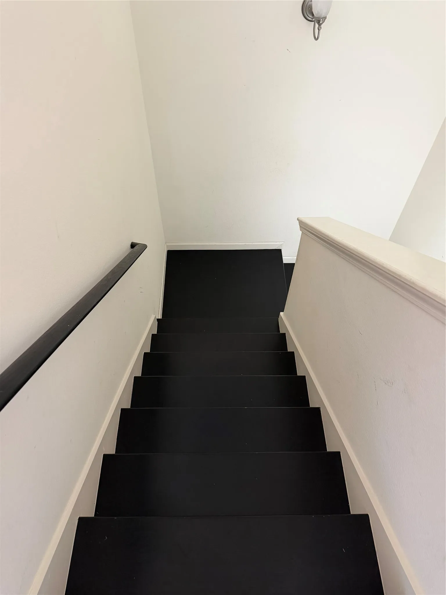 Stairwell featuring a dark-toned staircase, white walls, and a wall-mounted light fixture