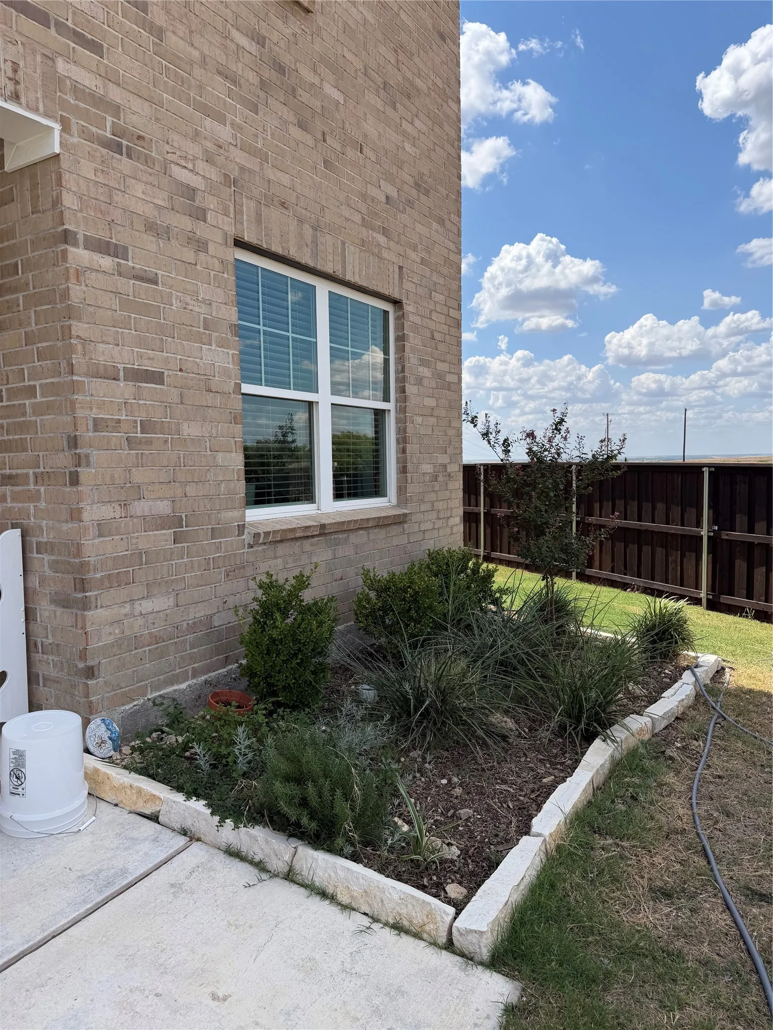 Brick exterior, white-framed window, landscaped garden bed, stone garden edging, wood privacy fence