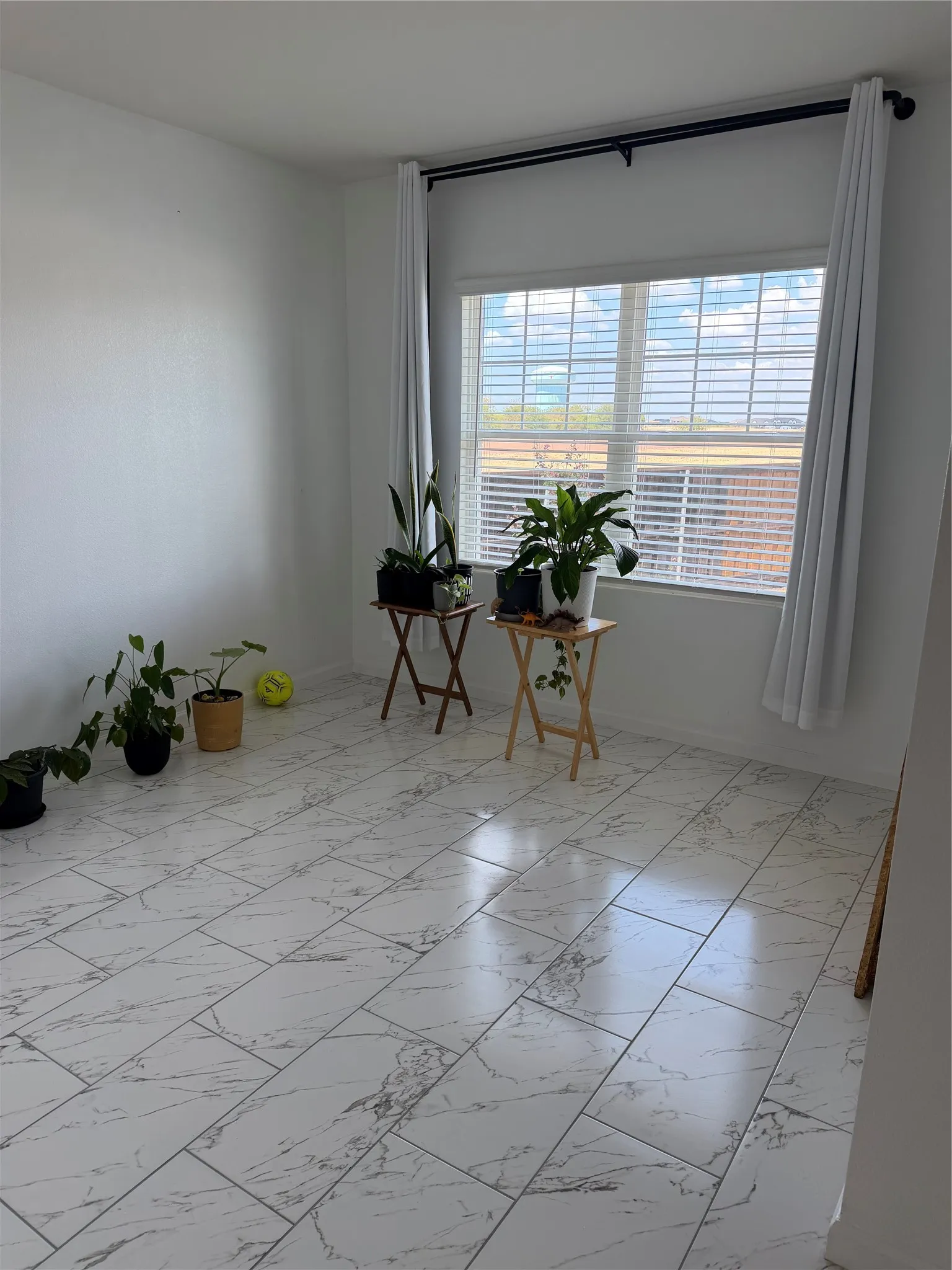 White tile flooring with a marble-effect pattern, large window with horizontal blinds, and white wall finishes