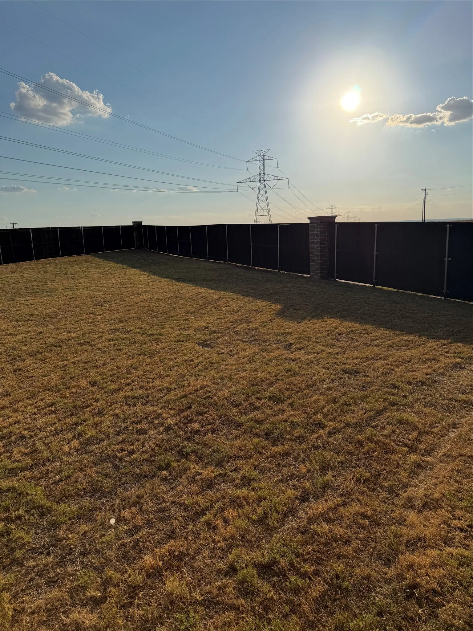 Expansive grass area with a privacy fence featuring brick pillars
