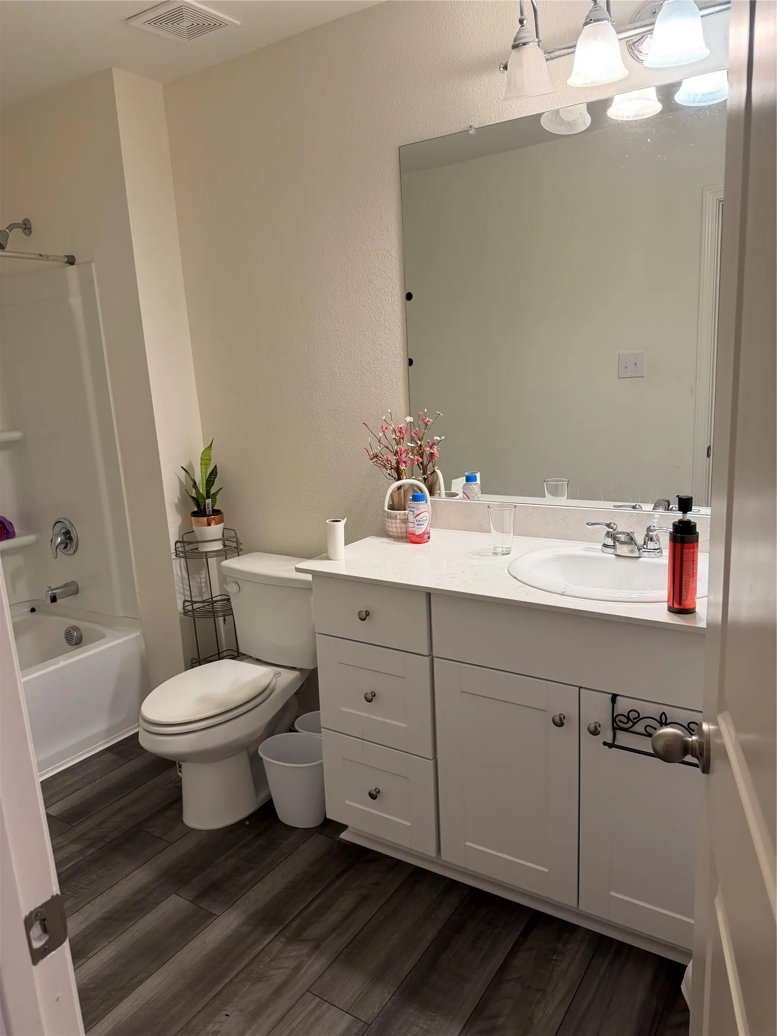 Bathroom featuring wood-finish flooring, a white vanity with integrated sink, a full-width mirror, and a built-in bathtub with shower