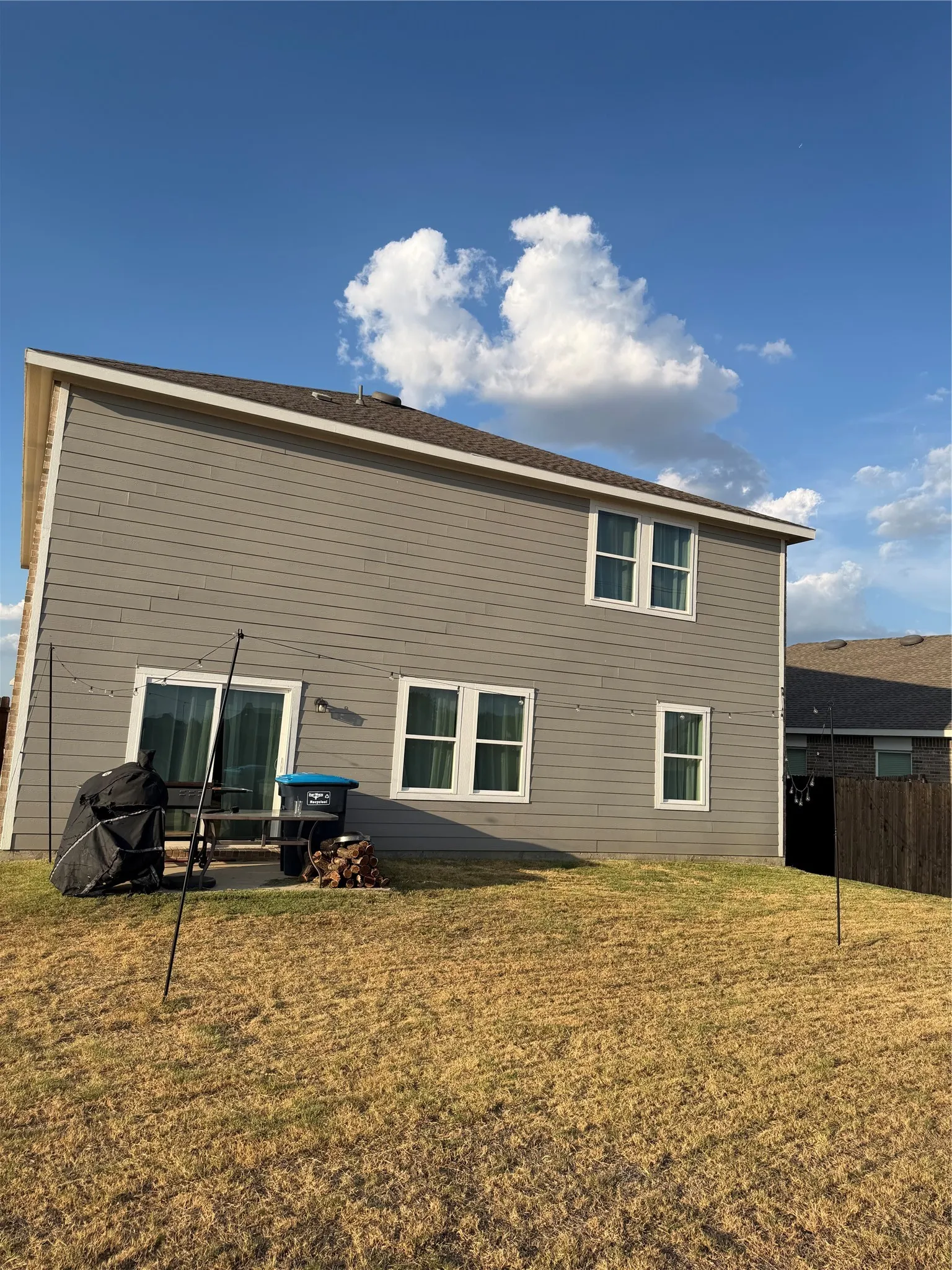 Gray siding exterior with multiple windows, a sliding glass door, and a concrete patio